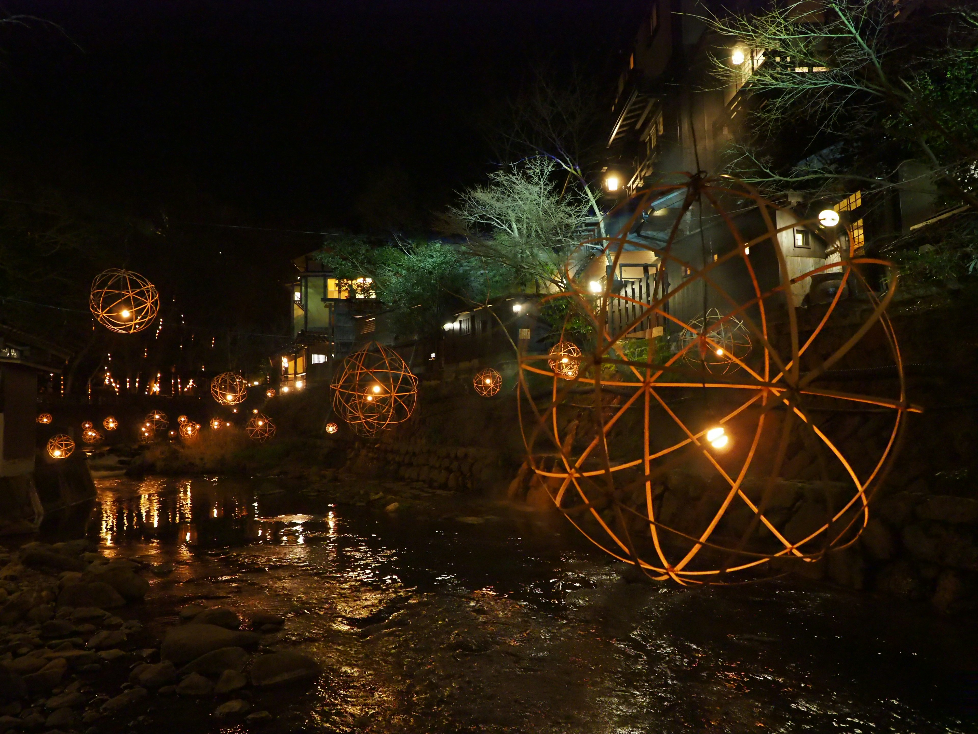 Illuminated spherical sculptures floating by a riverside at night