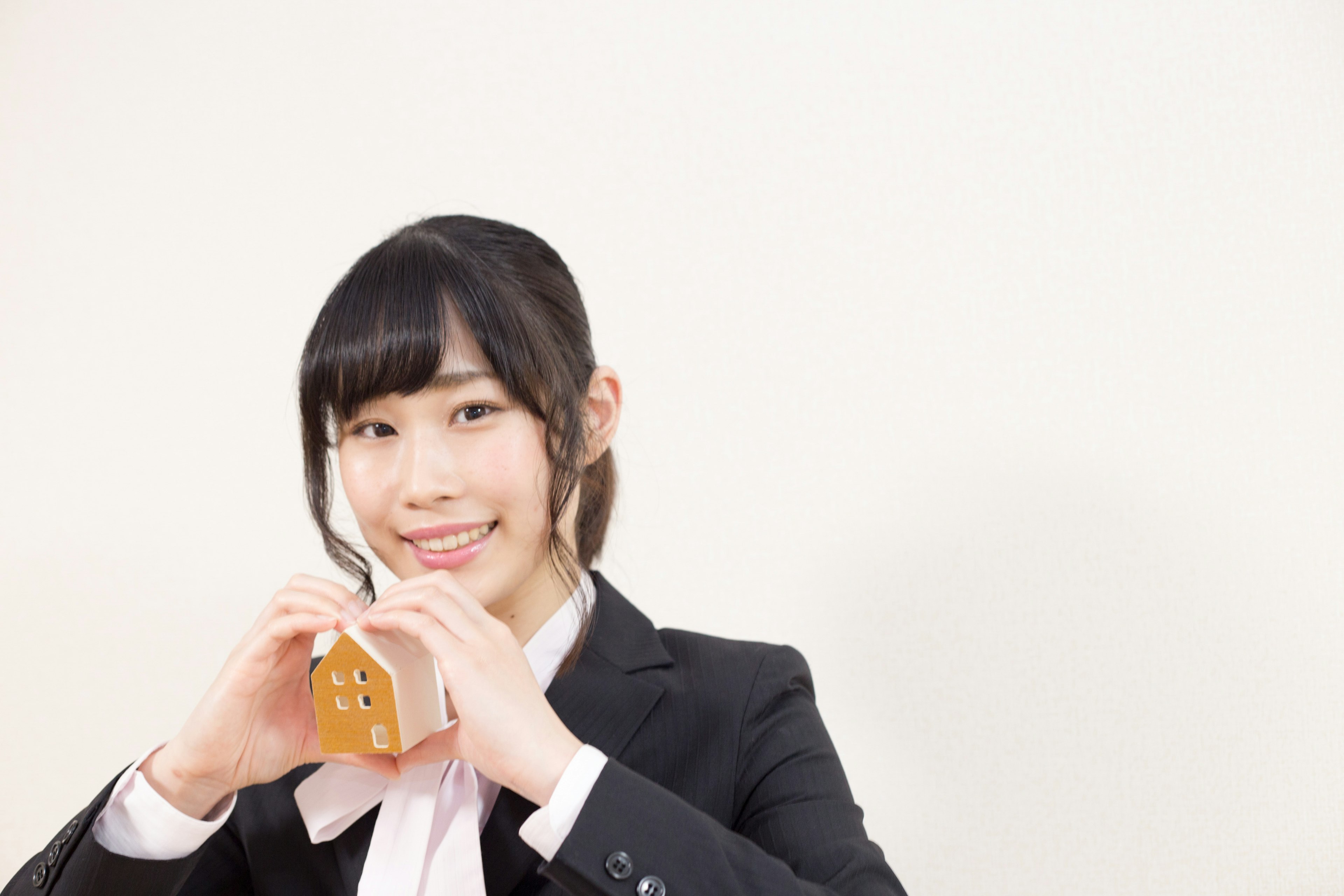 A woman in a suit smiling while holding a small object in a heart shape