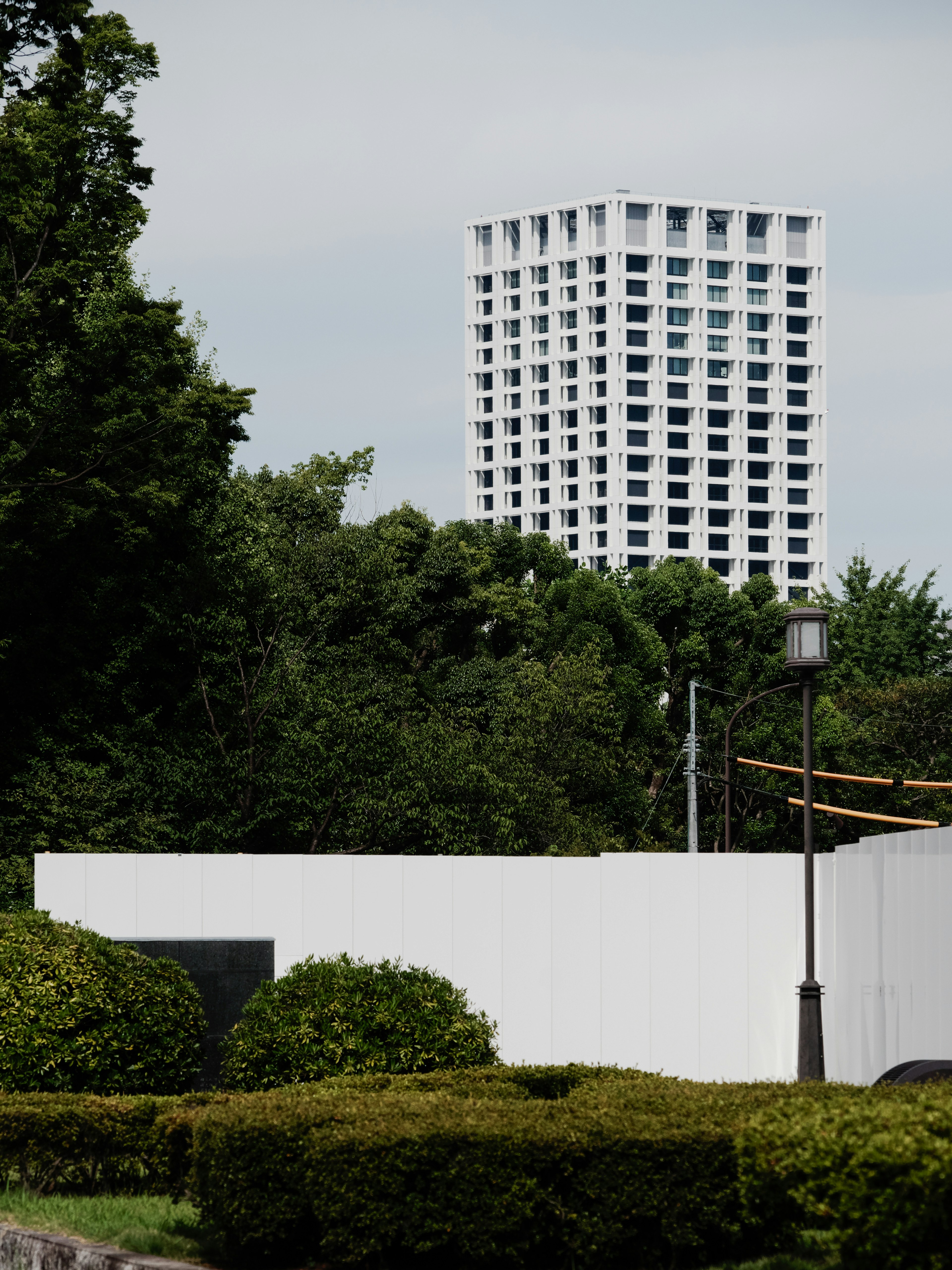 A modern high-rise building surrounded by greenery with a white structure in the foreground