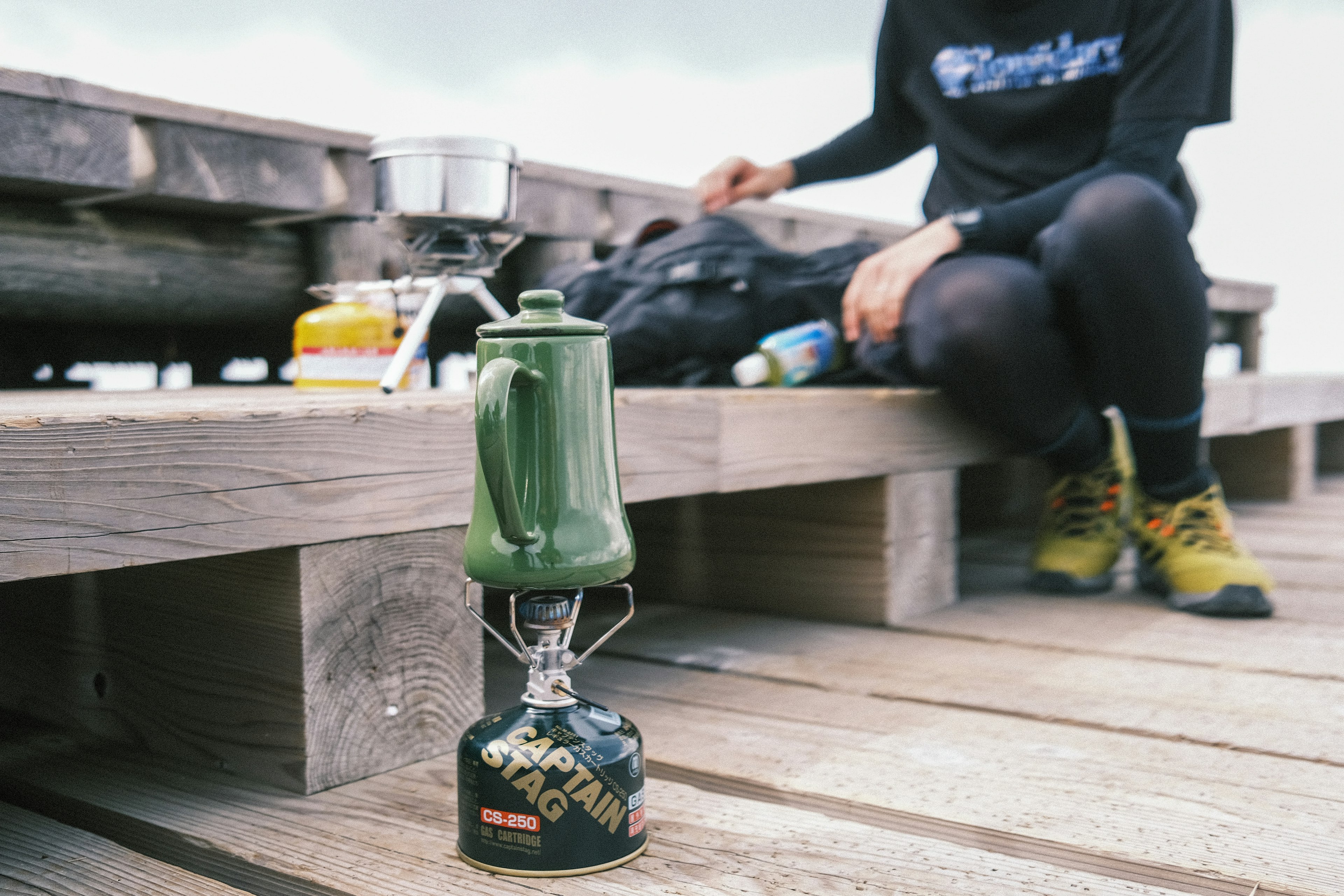 Une lanterne verte posée sur une terrasse en bois avec une personne qui cuisine à proximité