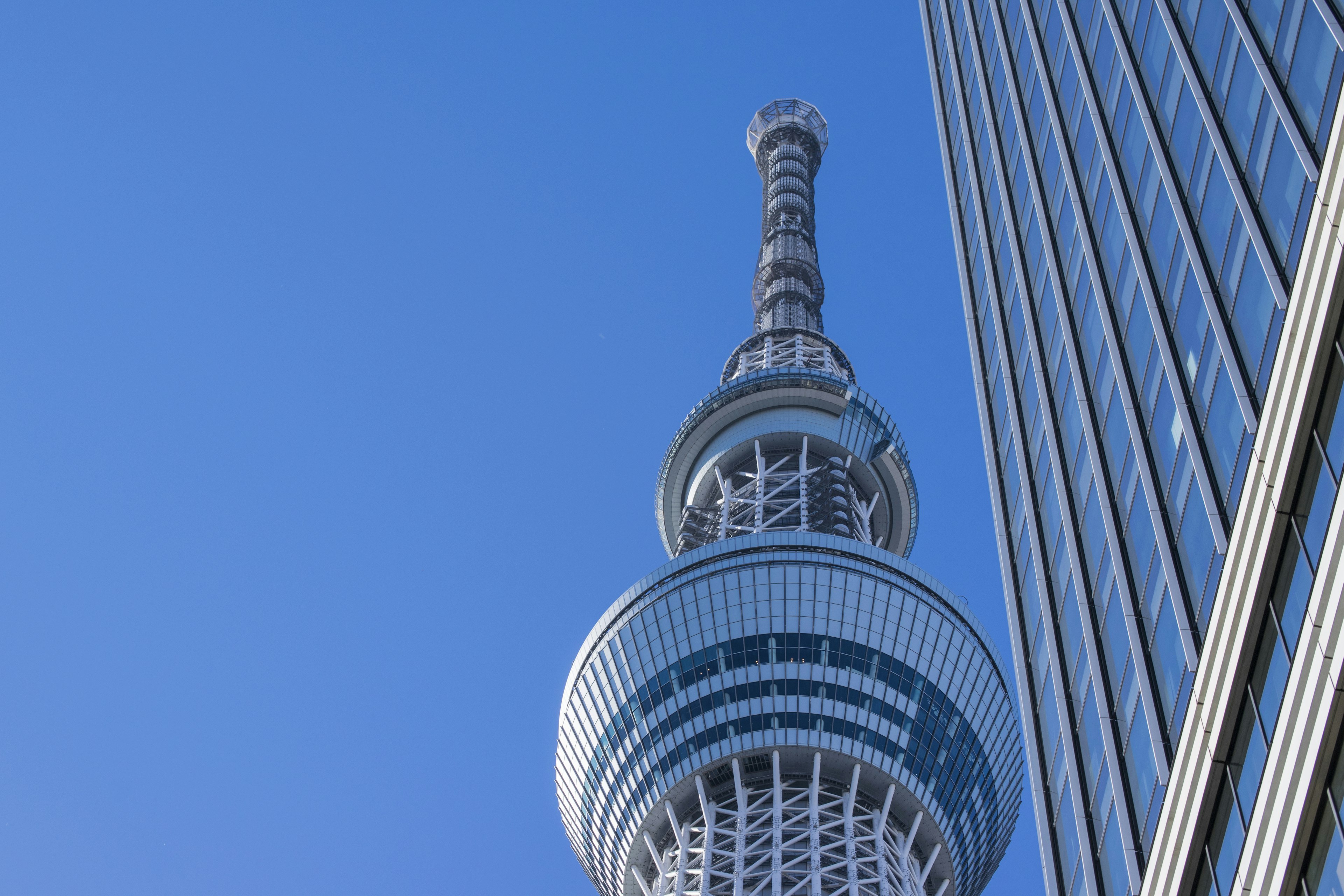 La parte superiore della Tokyo Skytree accanto a un edificio sotto un cielo blu chiaro