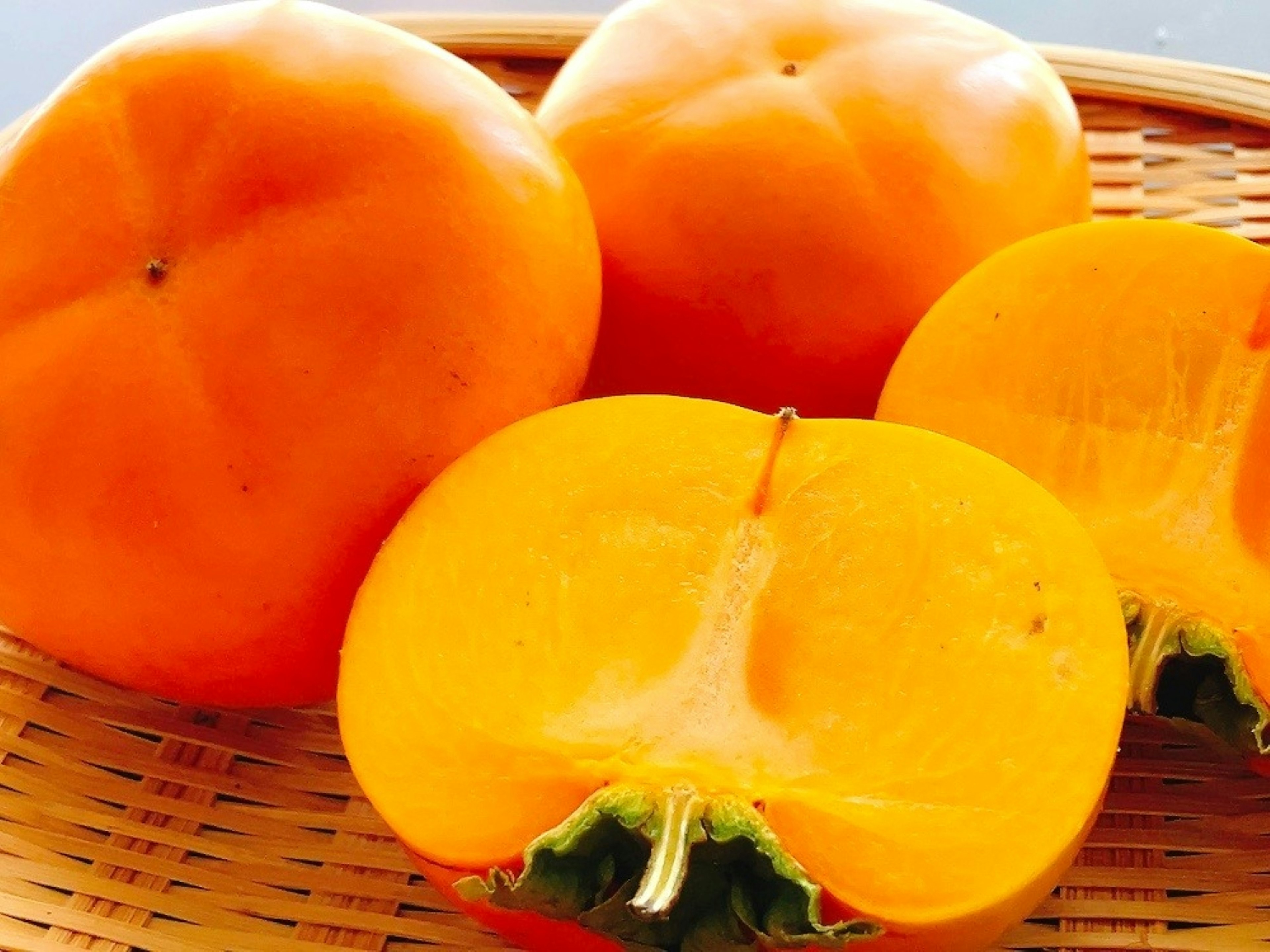 Image of orange persimmons in a basket with one cut in half