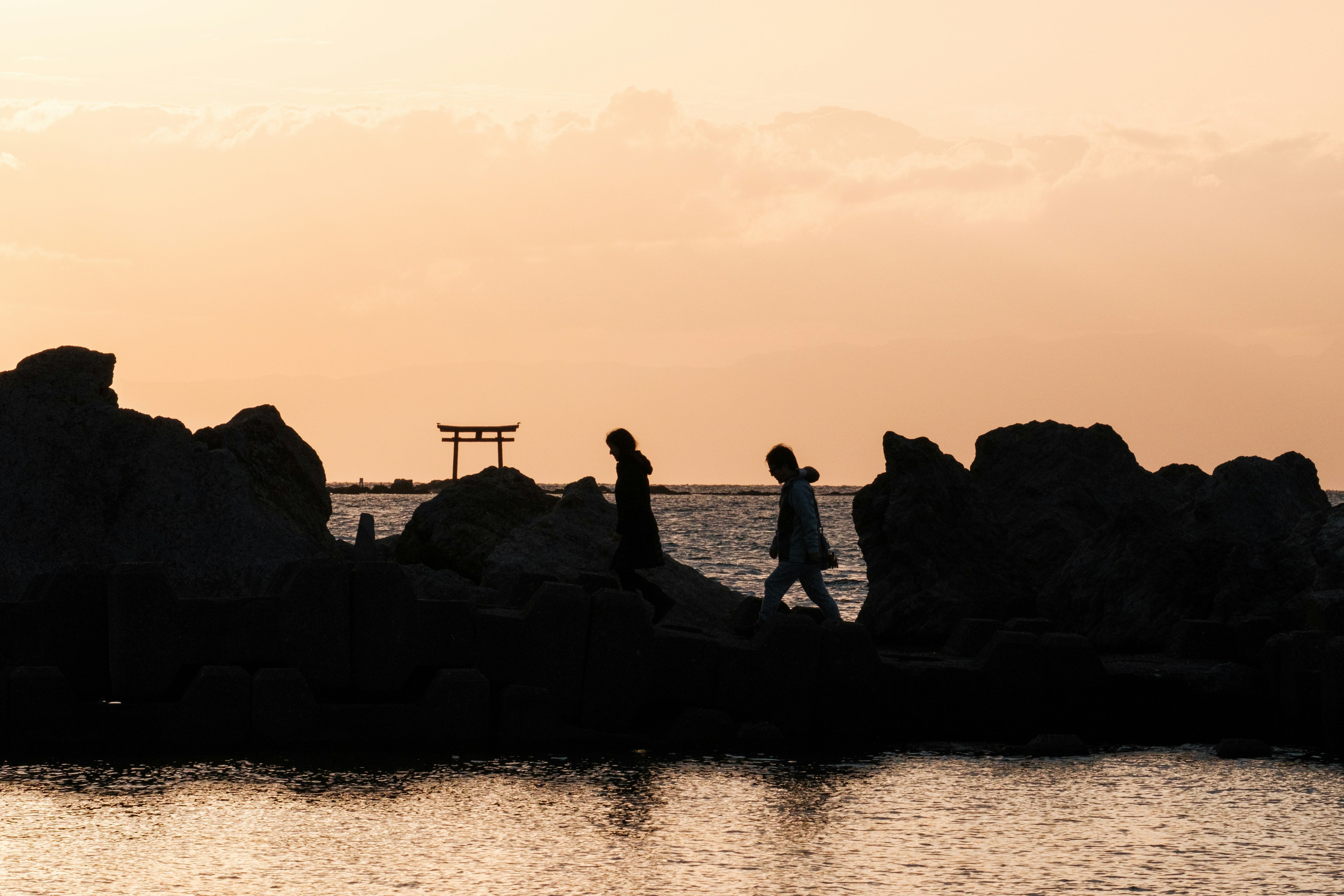 夕焼けの中、岩の上を歩く人々のシルエットと海の風景