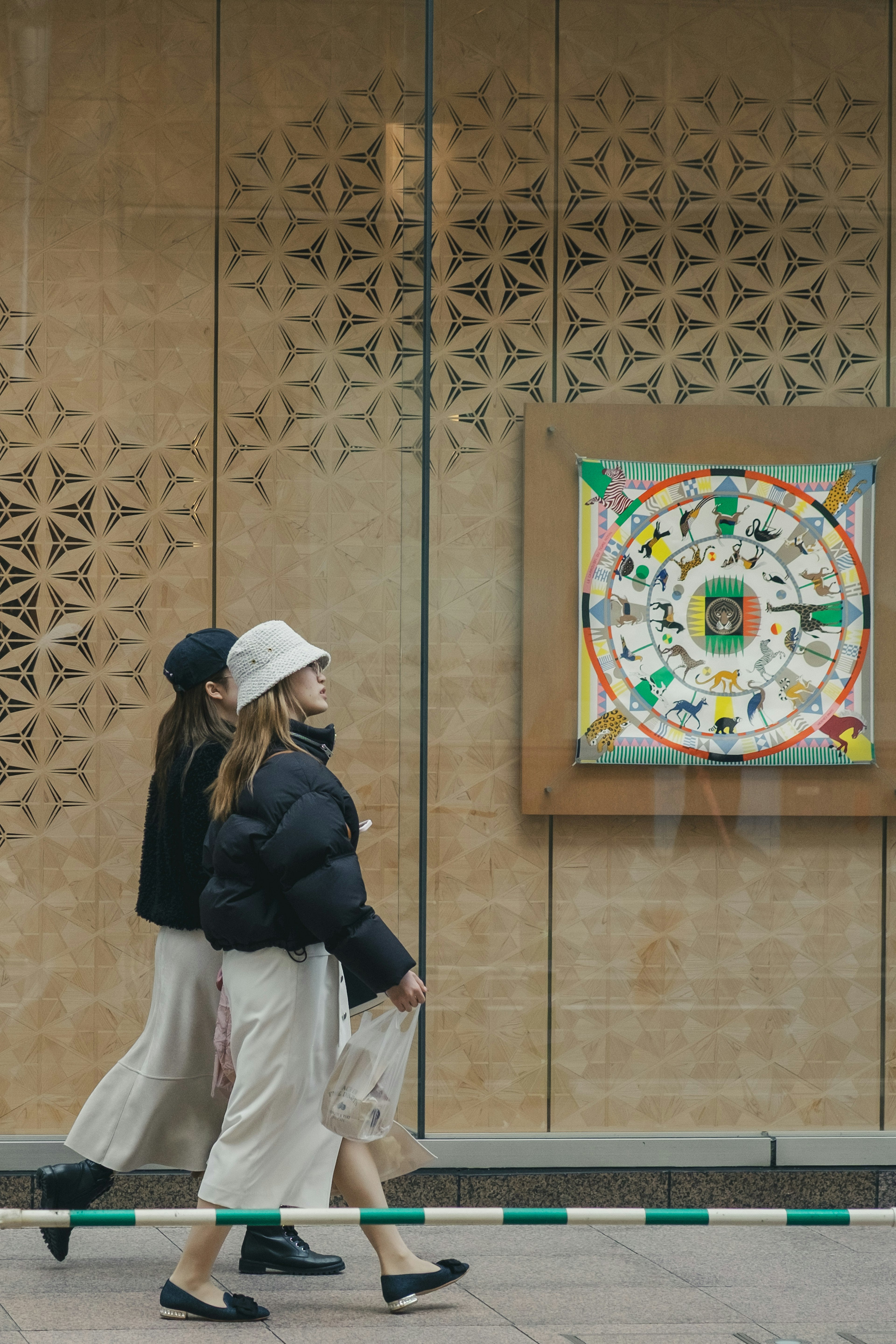 Dos mujeres caminando frente a una obra de arte con una pared decorativa al fondo