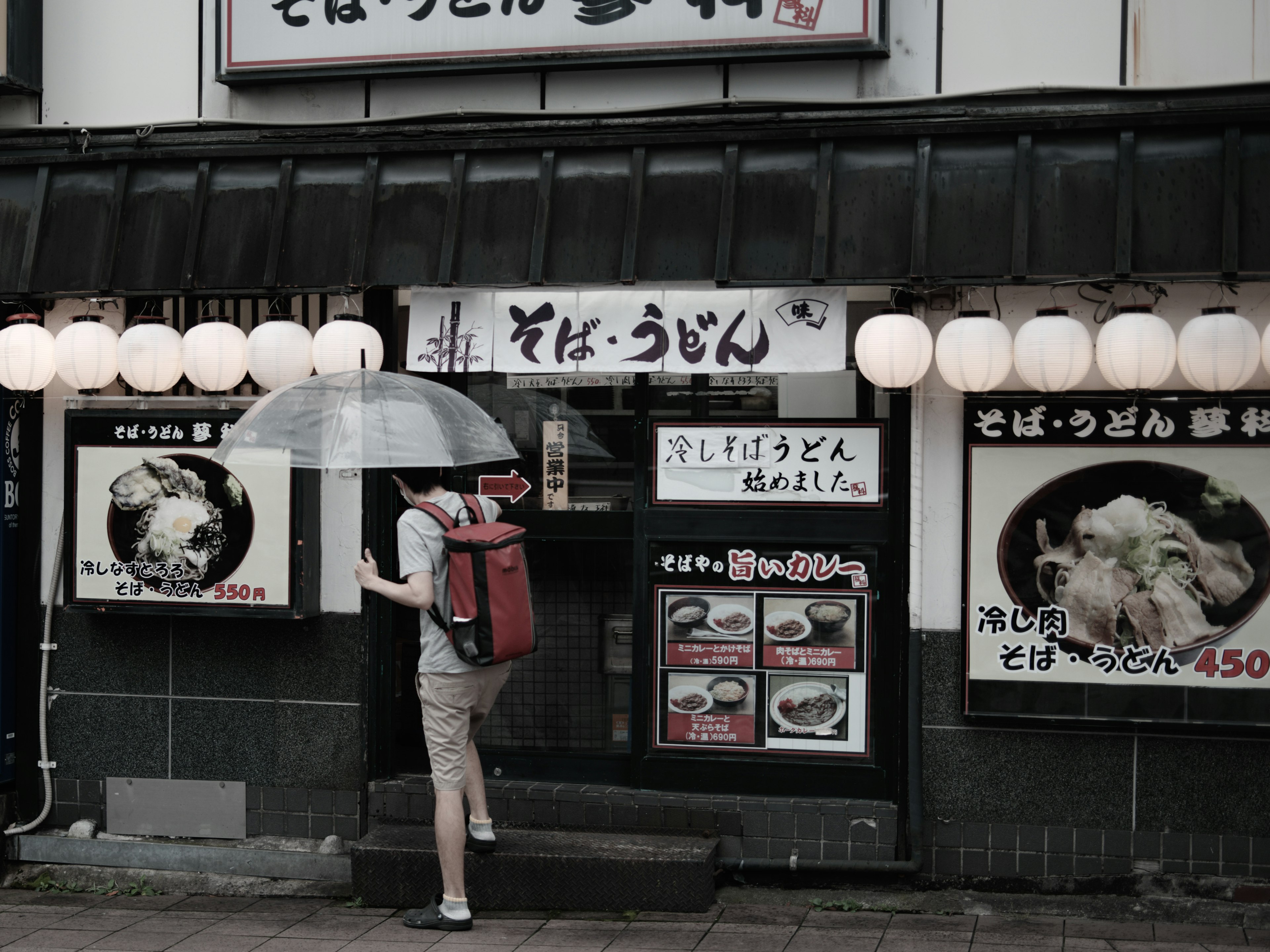 Personne entrant dans un restaurant de soba avec un parapluie sous la pluie