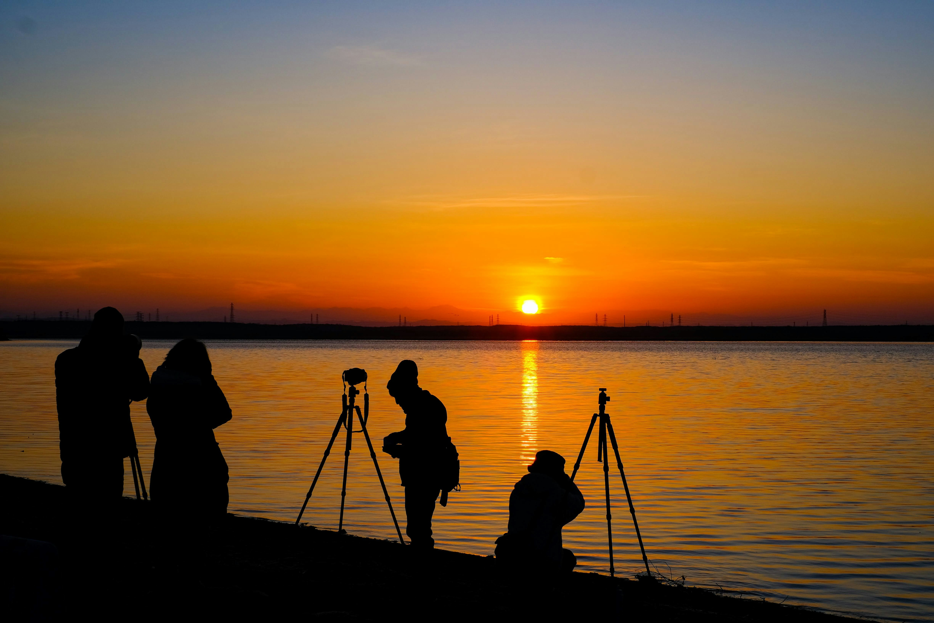 Silhouette di fotografi contro un tramonto vicino all'acqua