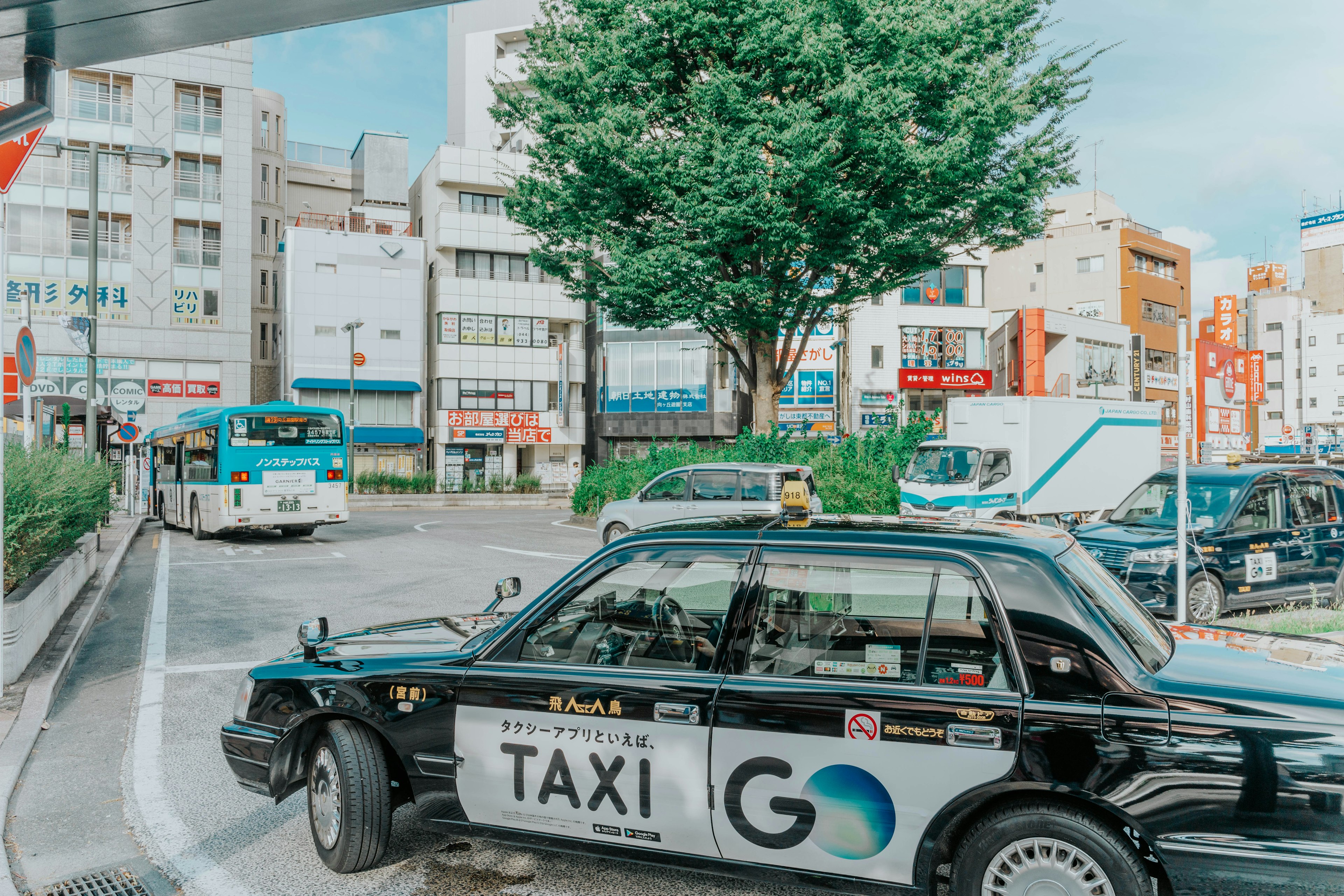 Black taxi driving on a city street with buildings and trees