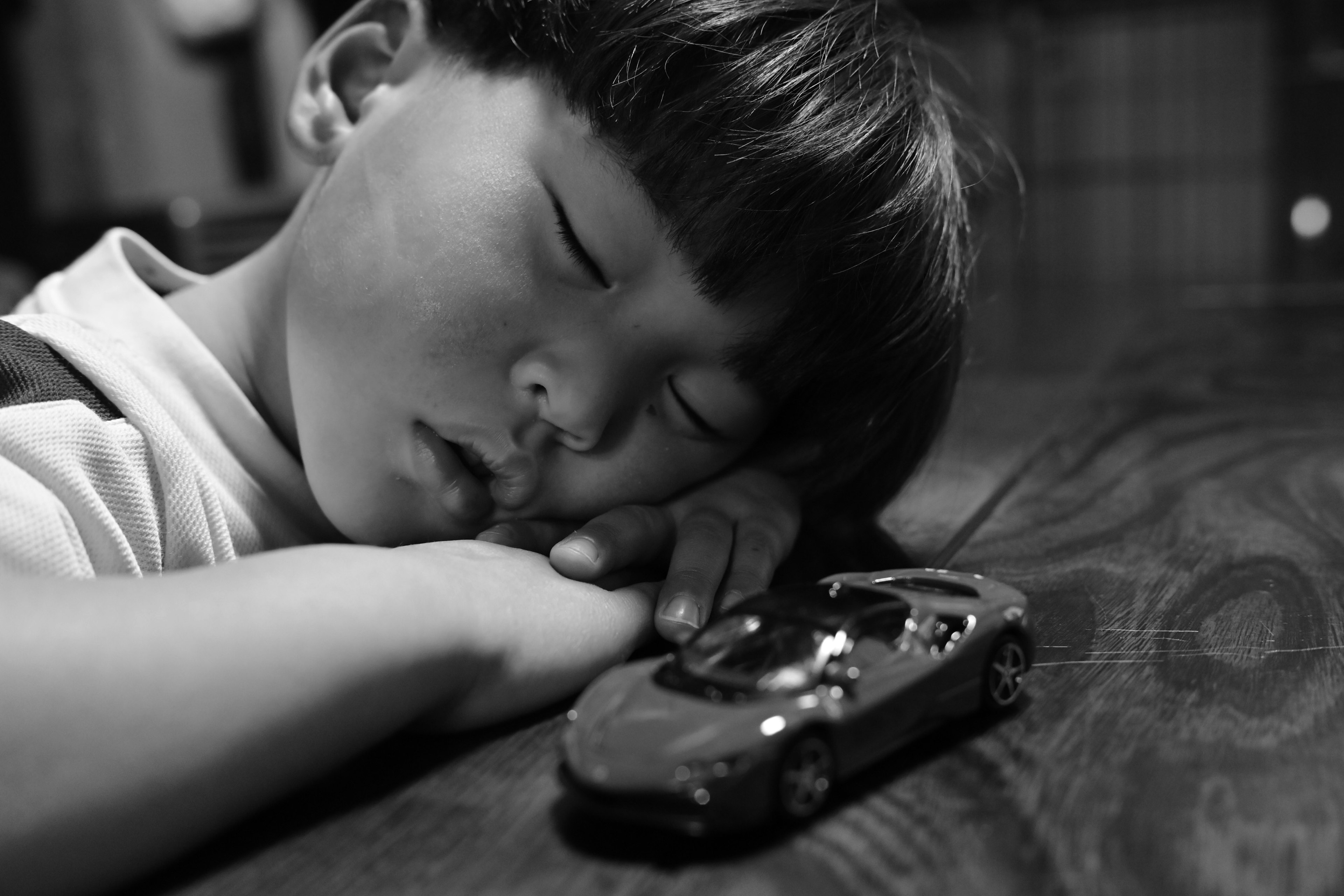 寝ている男の子とおもちゃの車の白黒写真