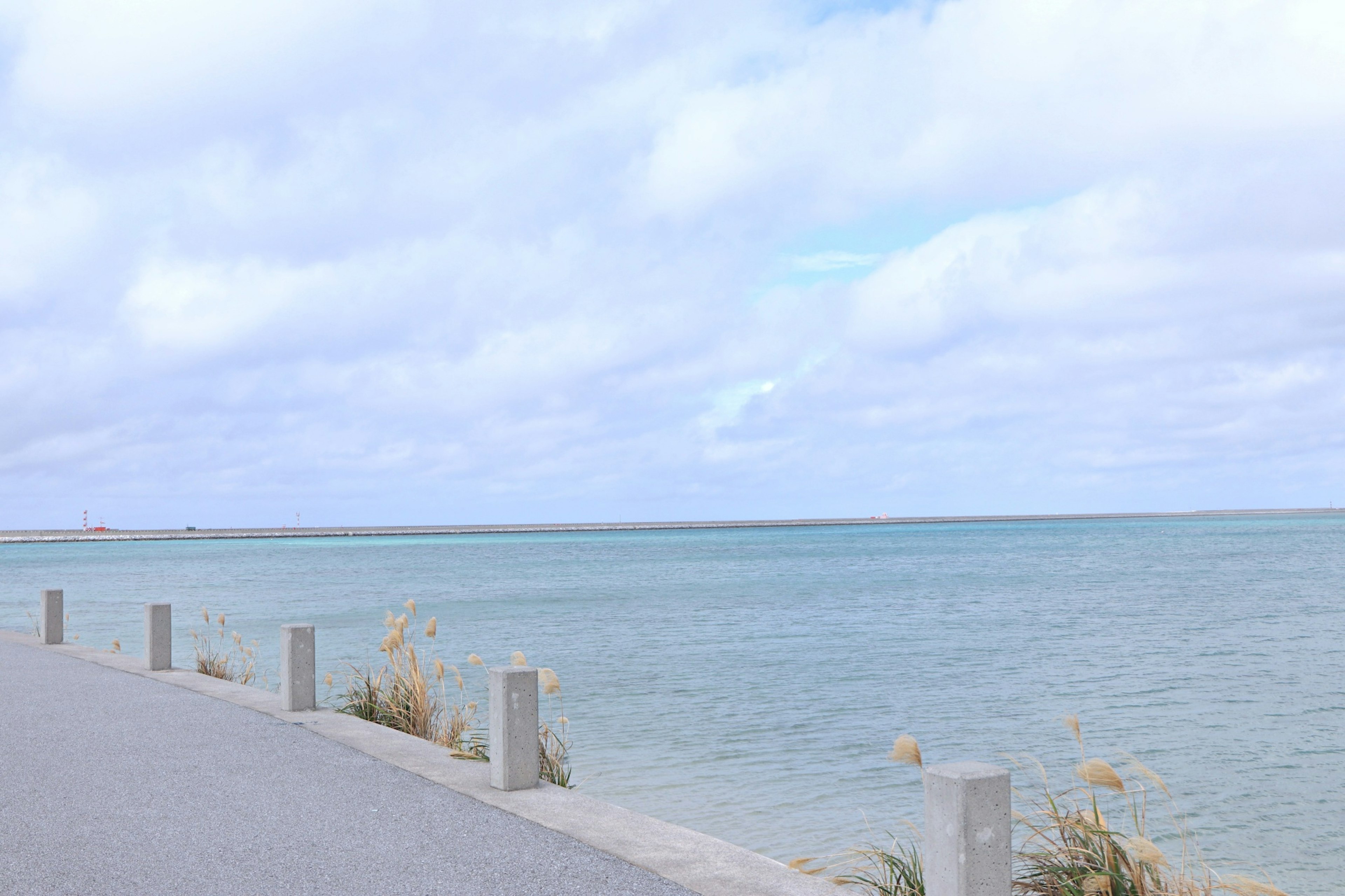 Vista panoramica del mare blu sotto un cielo nuvoloso con pilastri di cemento lungo la strada