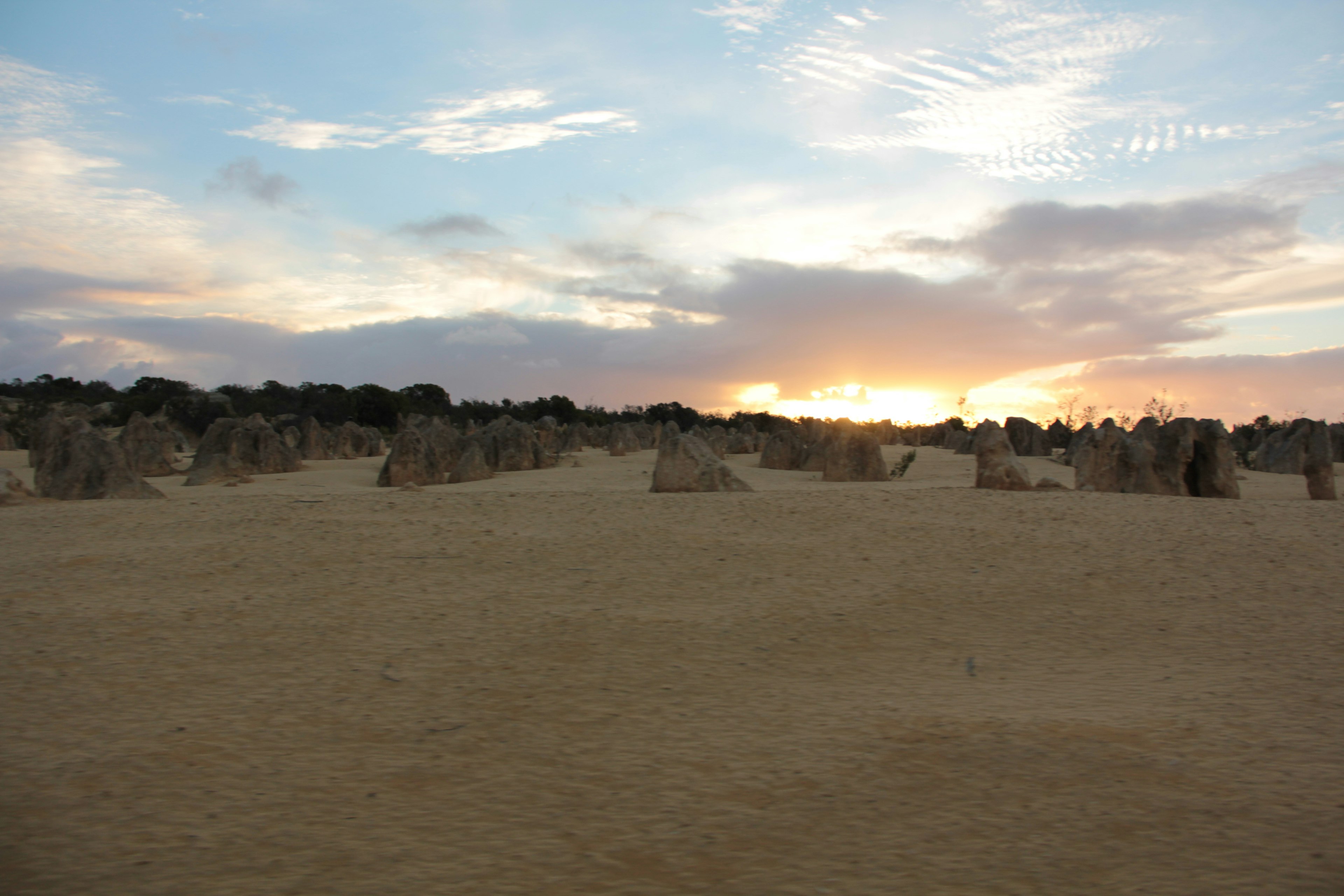 Weite Wüstenlandschaft mit Steinformationen im Hintergrund eines Sonnenaufgangs