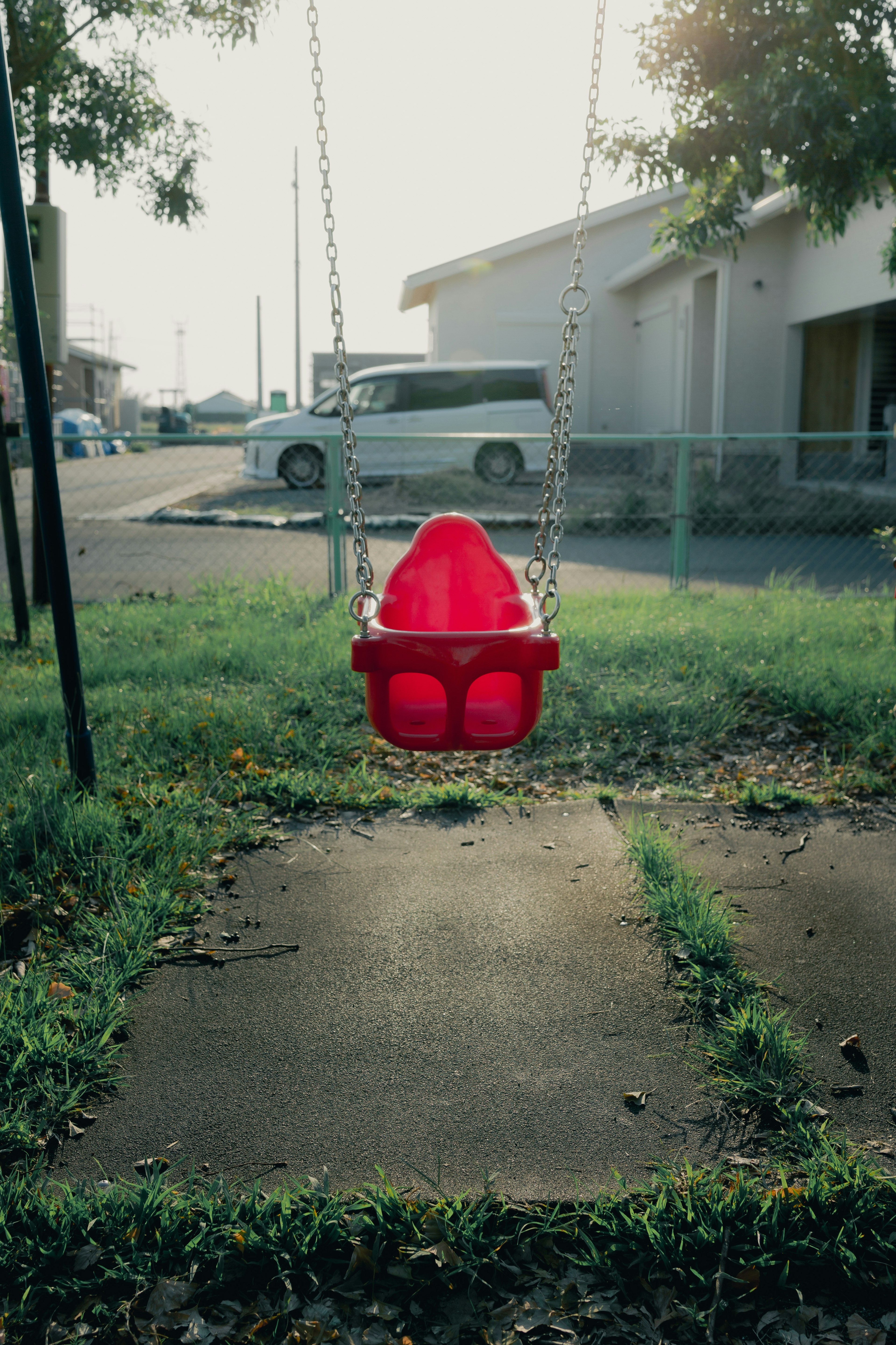 Red swing set in a playground with grass and pavement