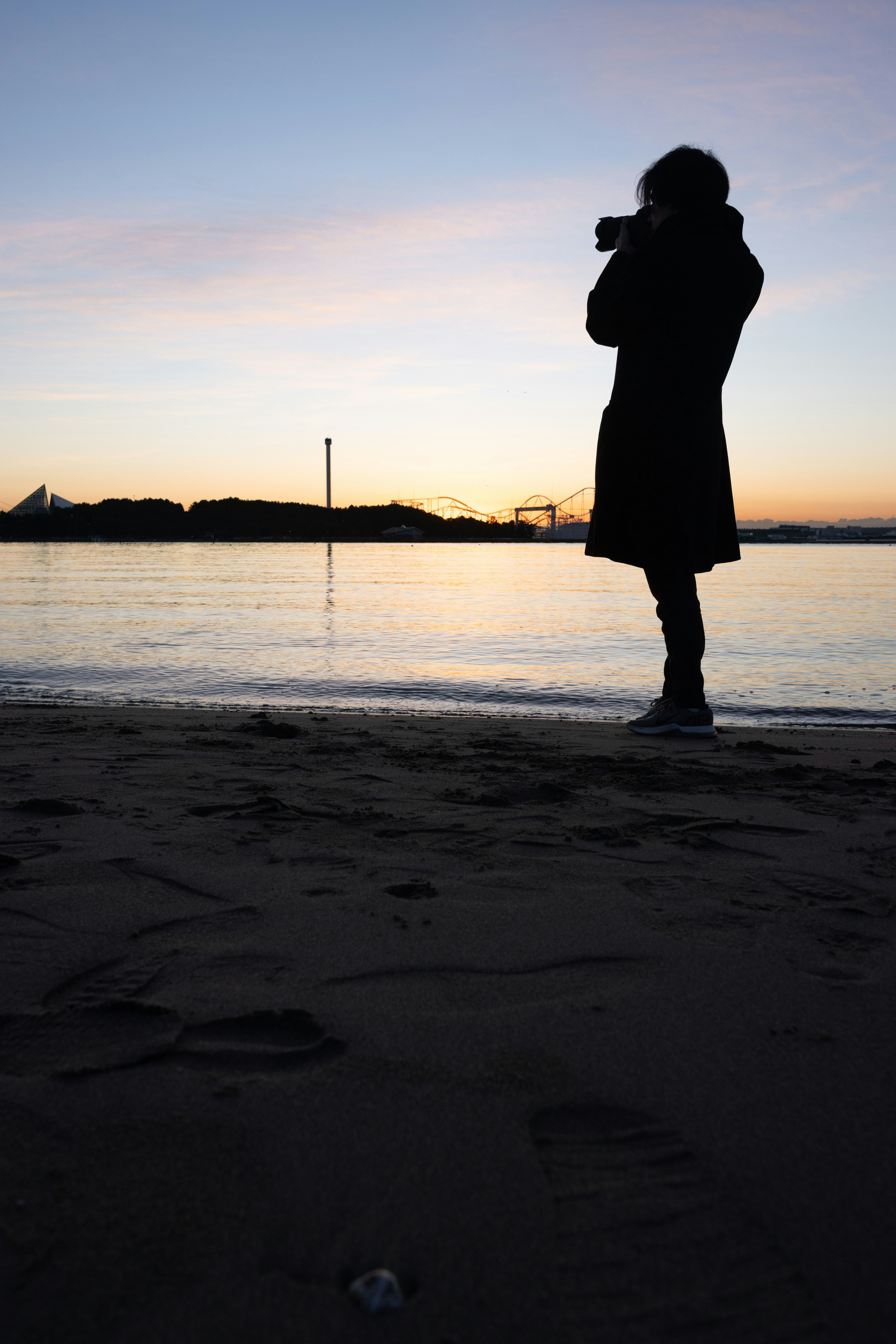 夕暮れ時に海辺でカメラを構える人物のシルエット