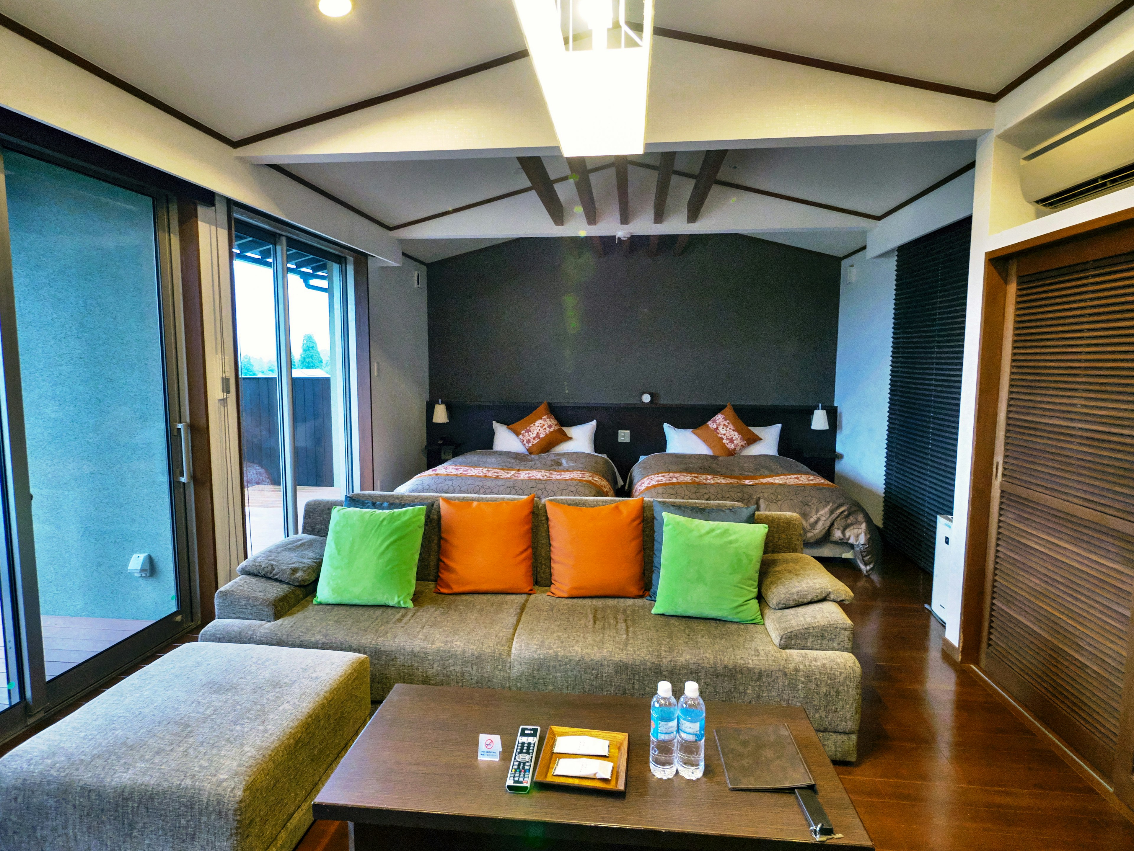 Modern hotel room featuring two double beds with colorful cushions and a cozy seating area