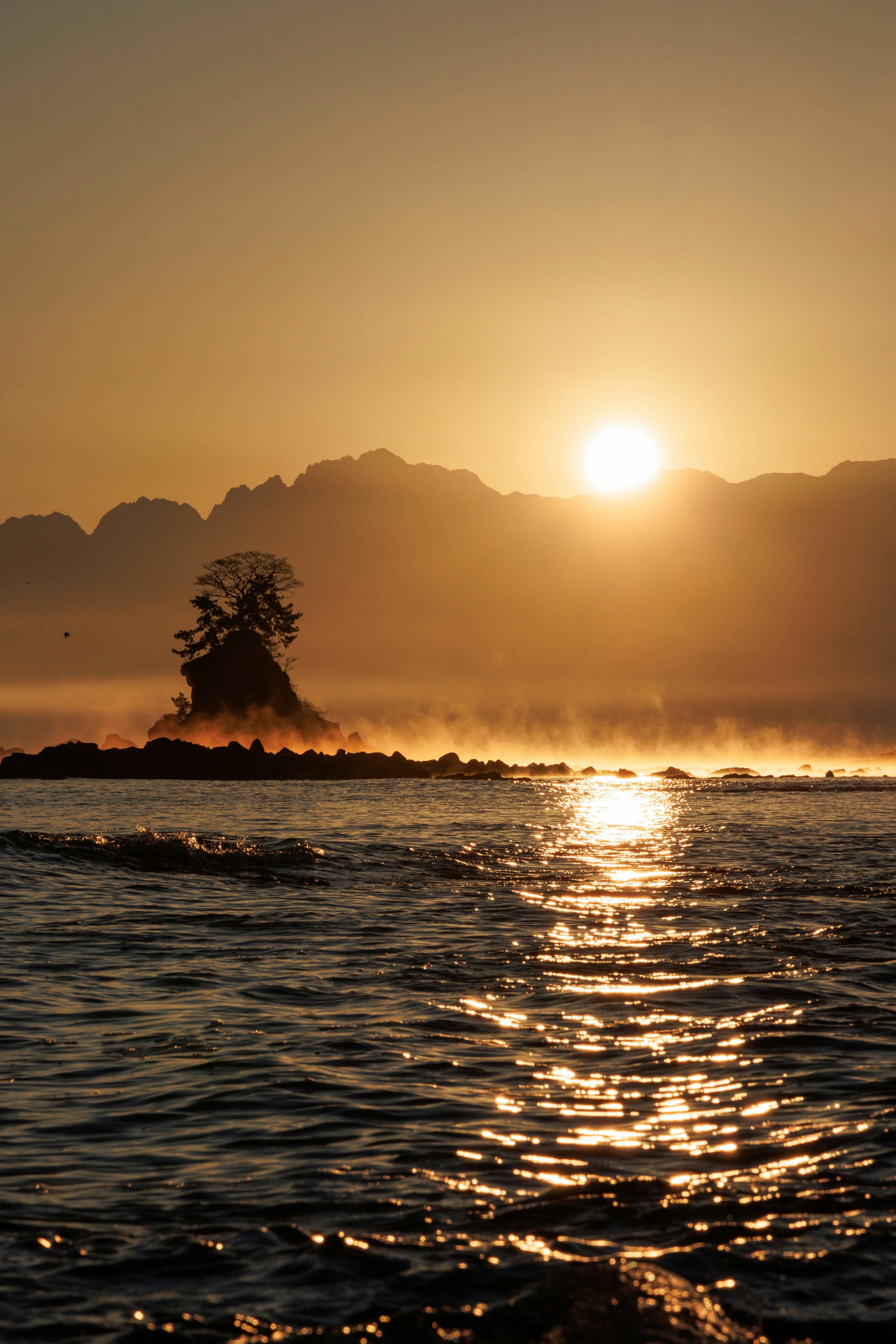 Schöne Sonnenaufgangslandschaft neblige Berge und Licht, das sich auf ruhigem Wasser spiegelt