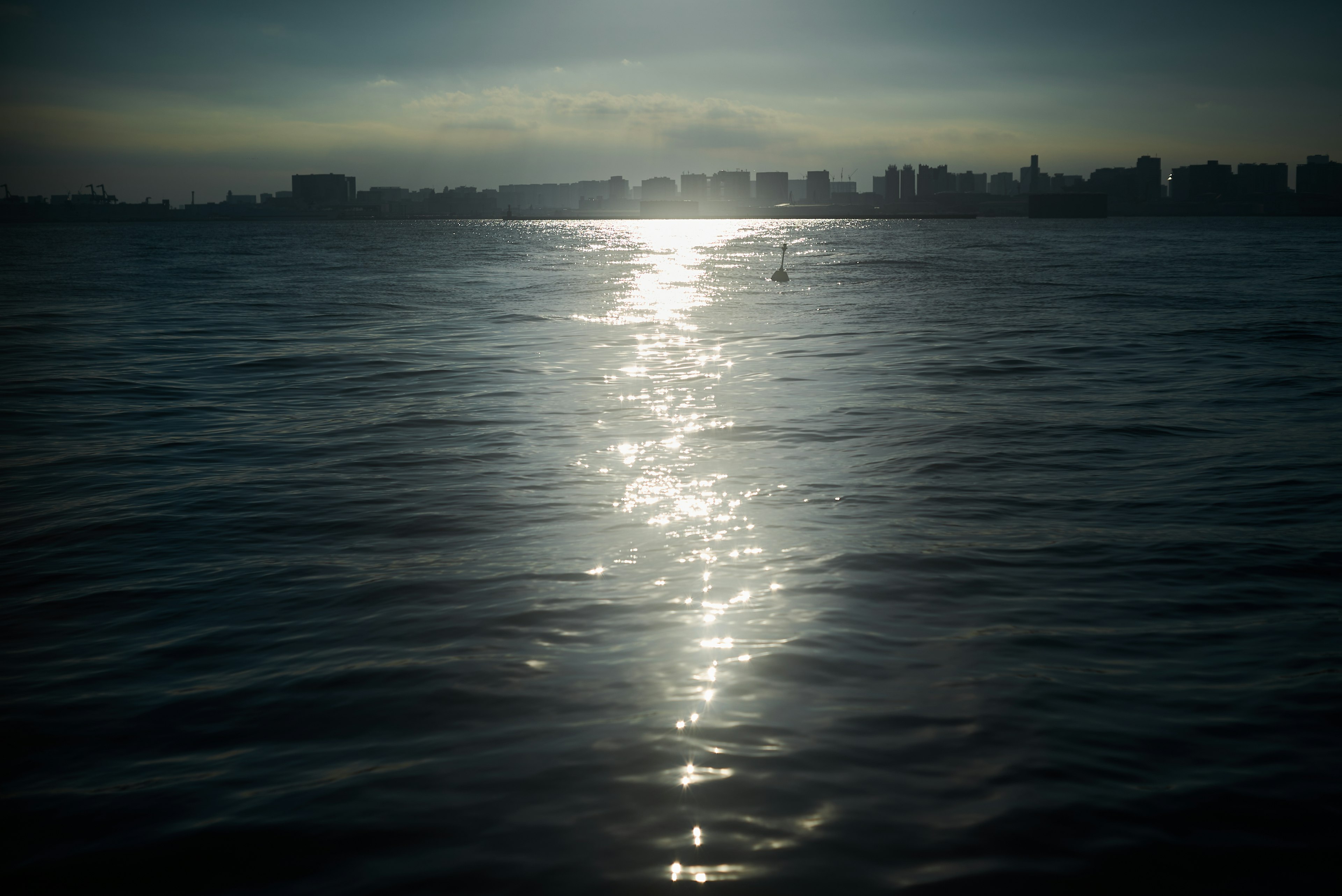 海の上に反射する光と薄暗い都市のシルエット