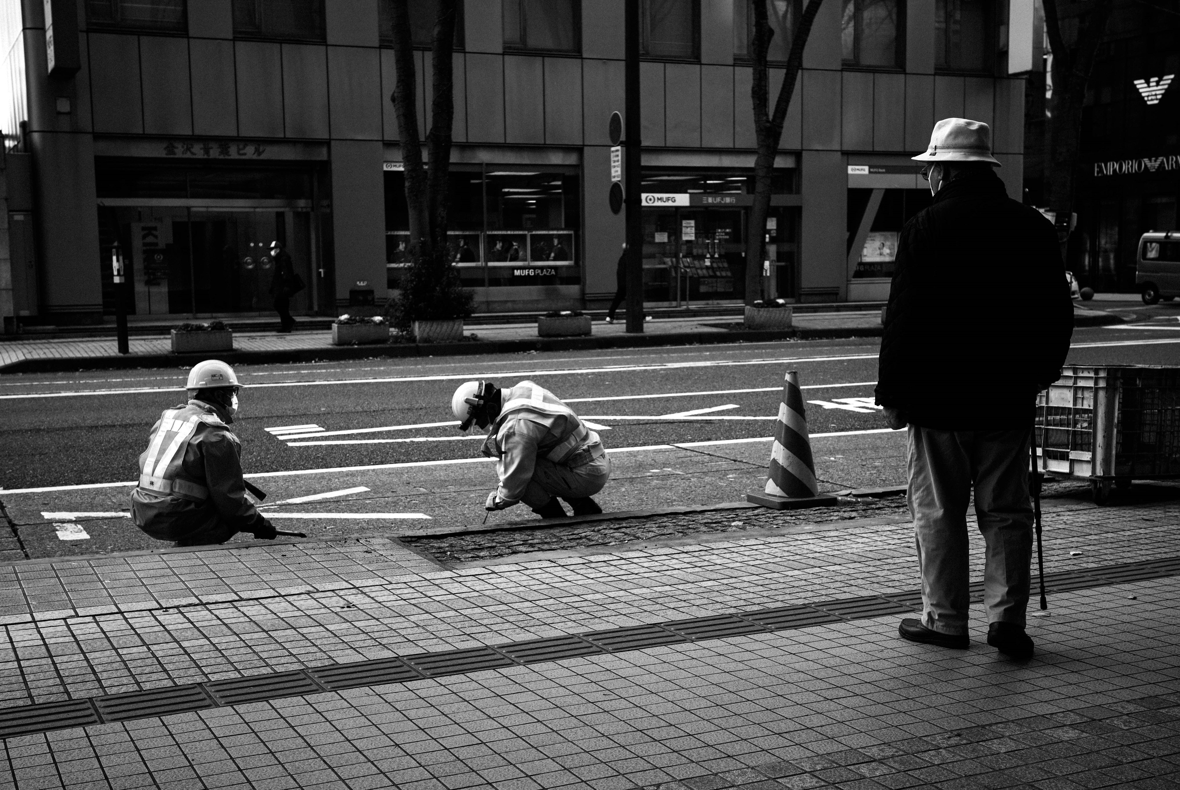 Trabajadores realizando mantenimiento en la calle mientras un transeúnte observa