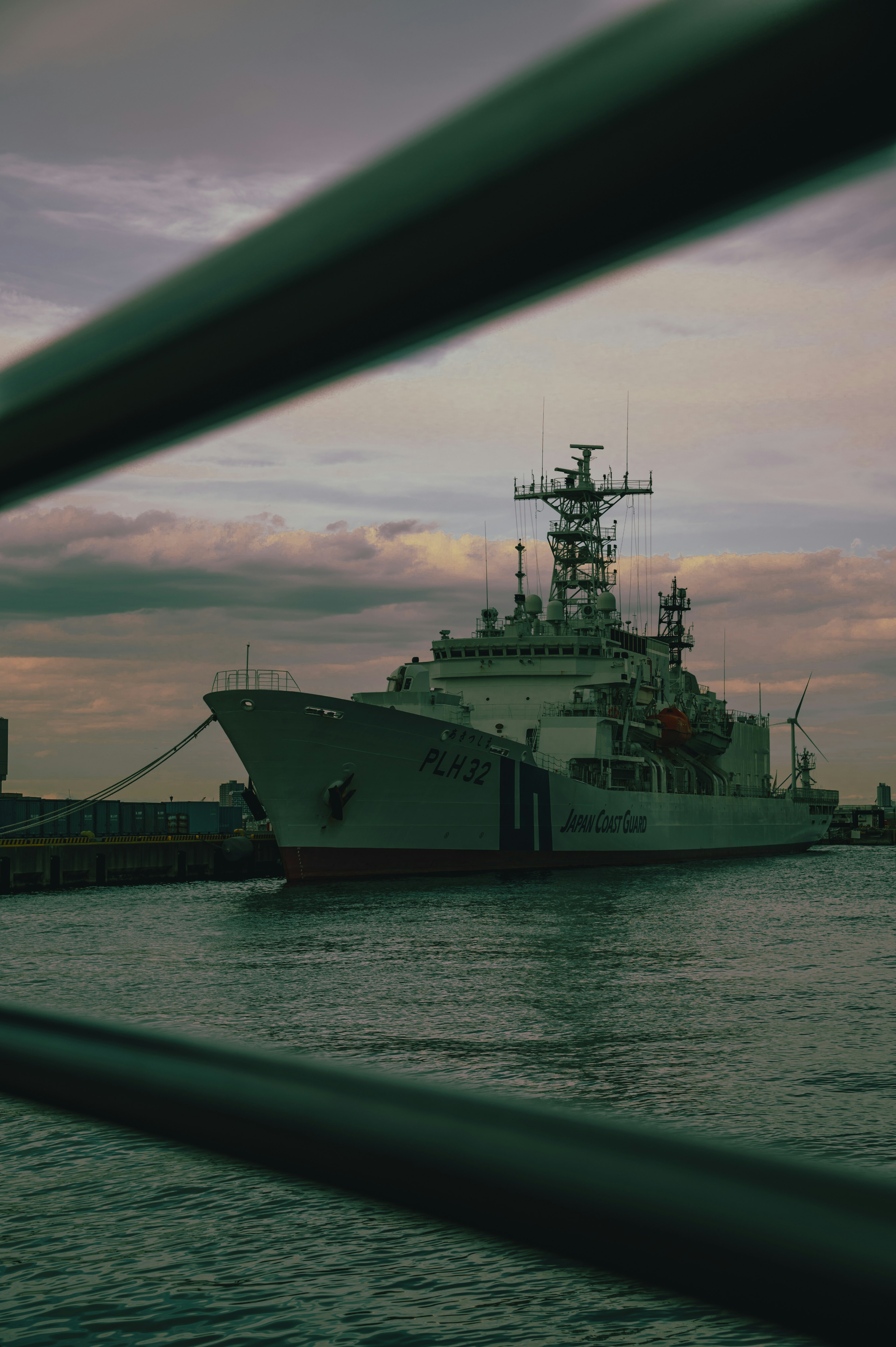 A naval ship docked at a port with a cloudy sky and calm water