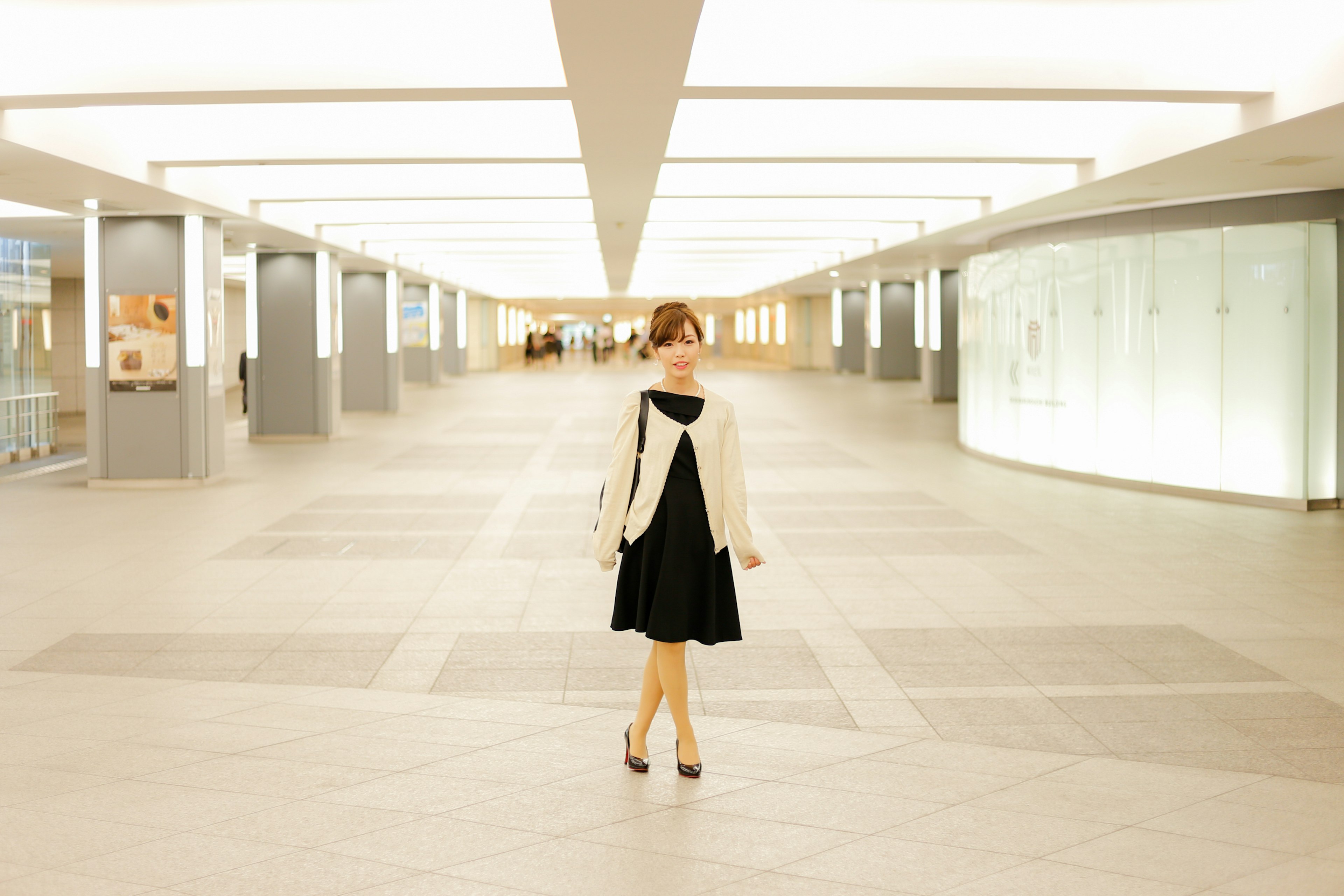 A woman standing in a spacious area wearing a black dress and a white jacket