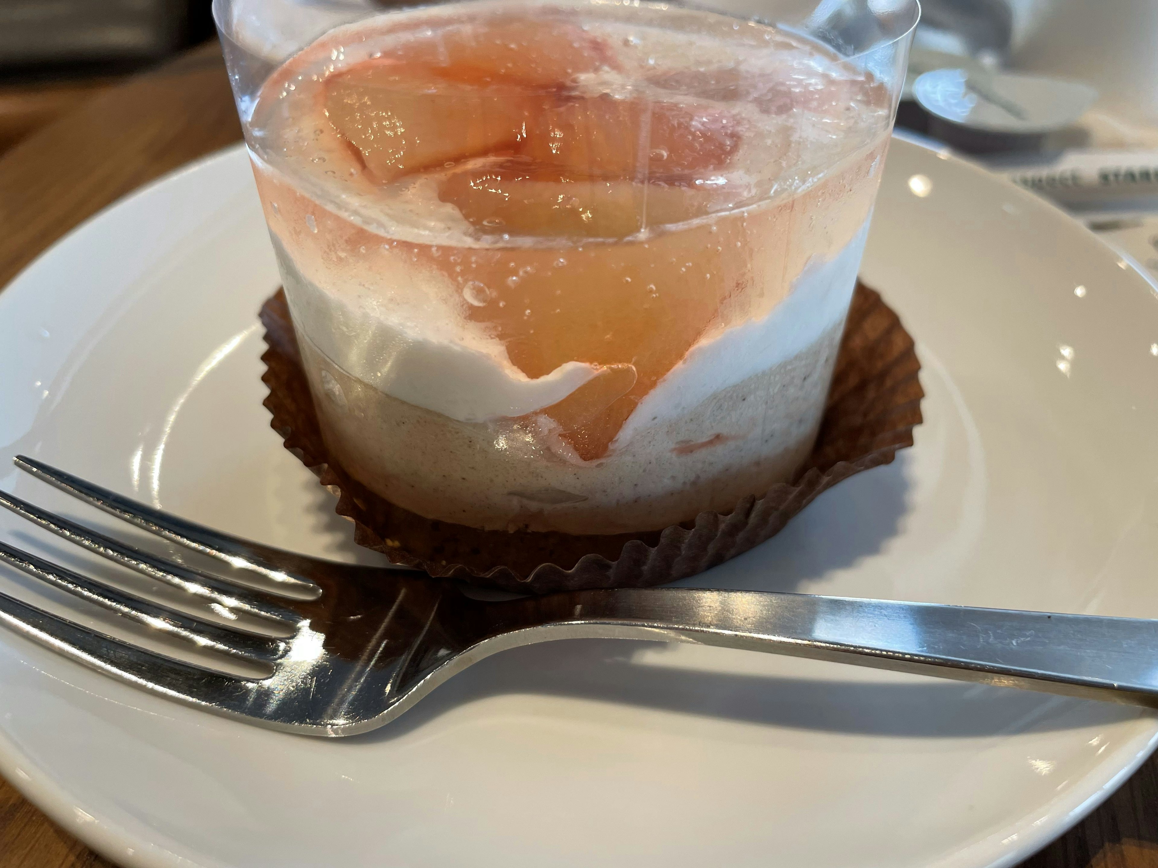 Dessert aux fruits en couches dans une tasse transparente avec des tranches de pêche sur le dessus et une couche de crème sur une tasse en chocolat dans une assiette blanche