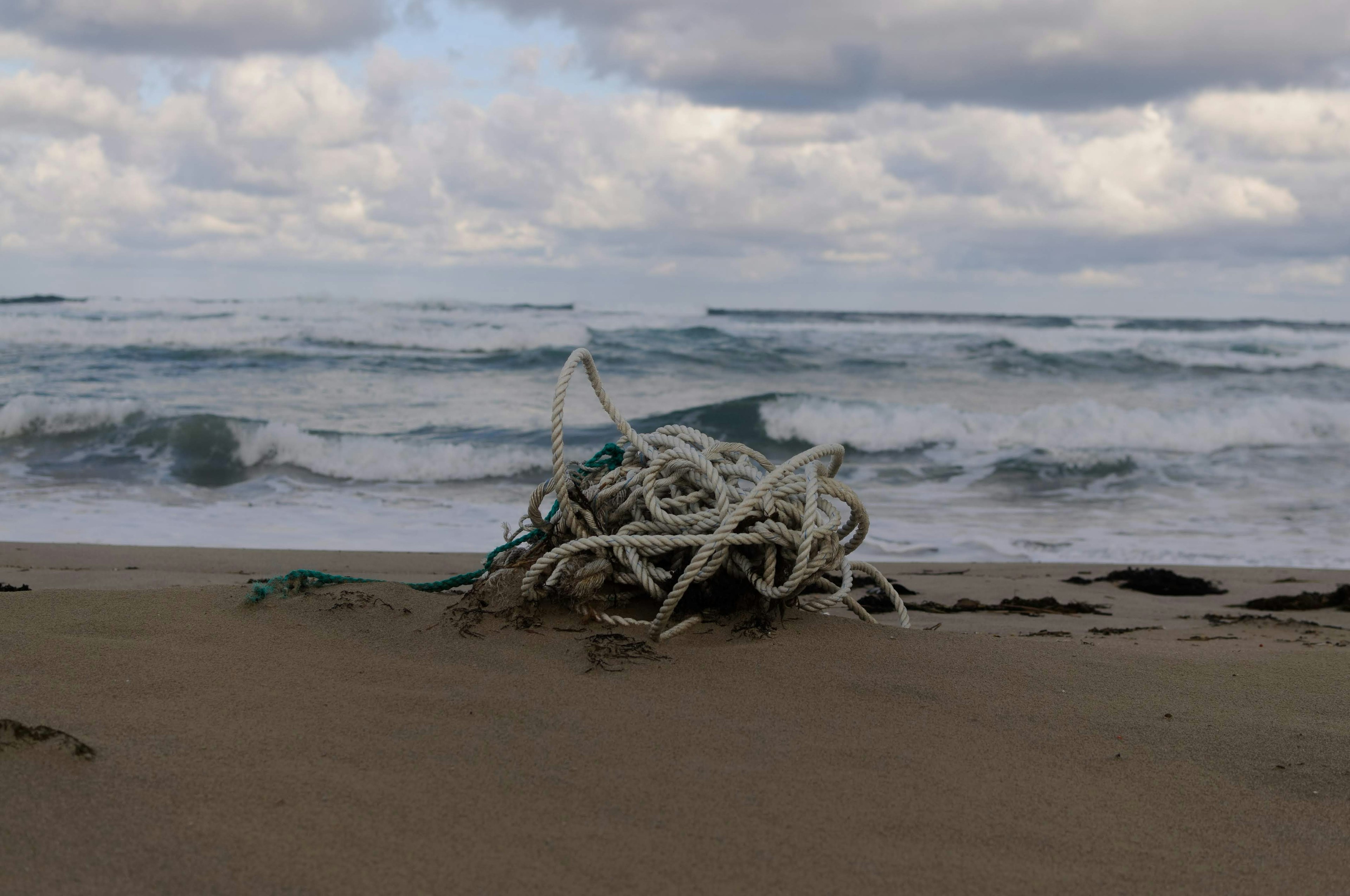 Cordes blanches emmêlées échouées sur une plage de sable avec des vagues agitées