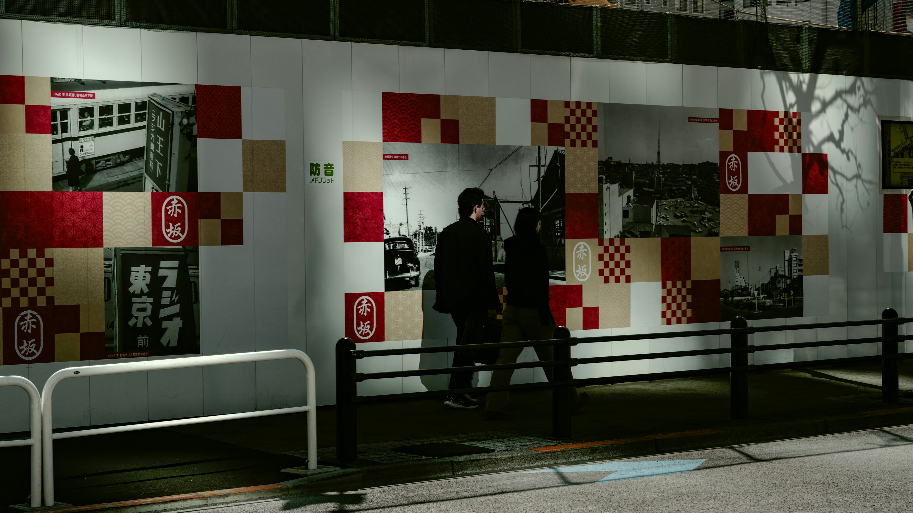 Silhouettes de personnes marchant le long d'une rue avec un mur à motifs rouges et blancs