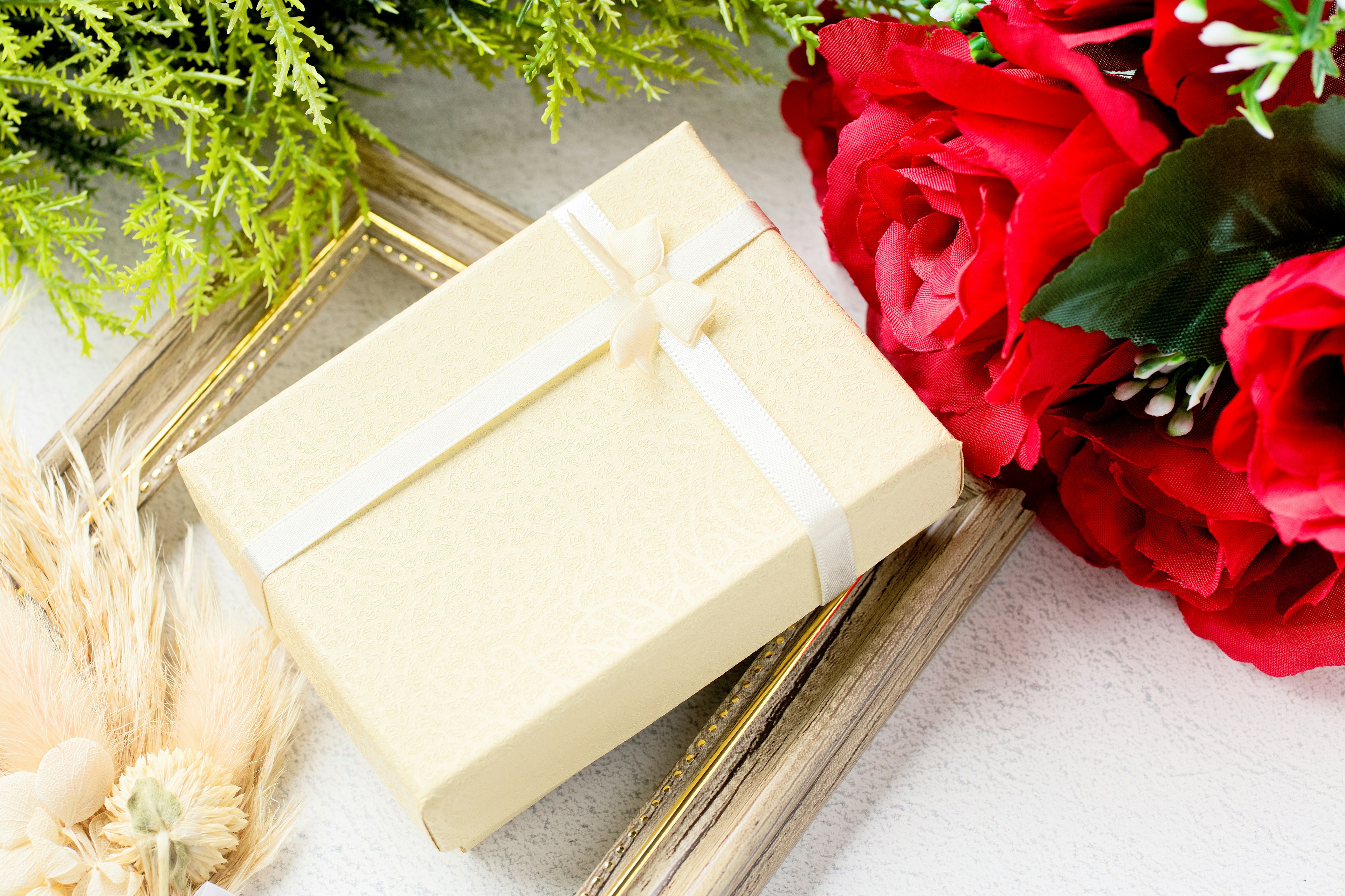 Cream-colored gift box surrounded by red roses and green leaves