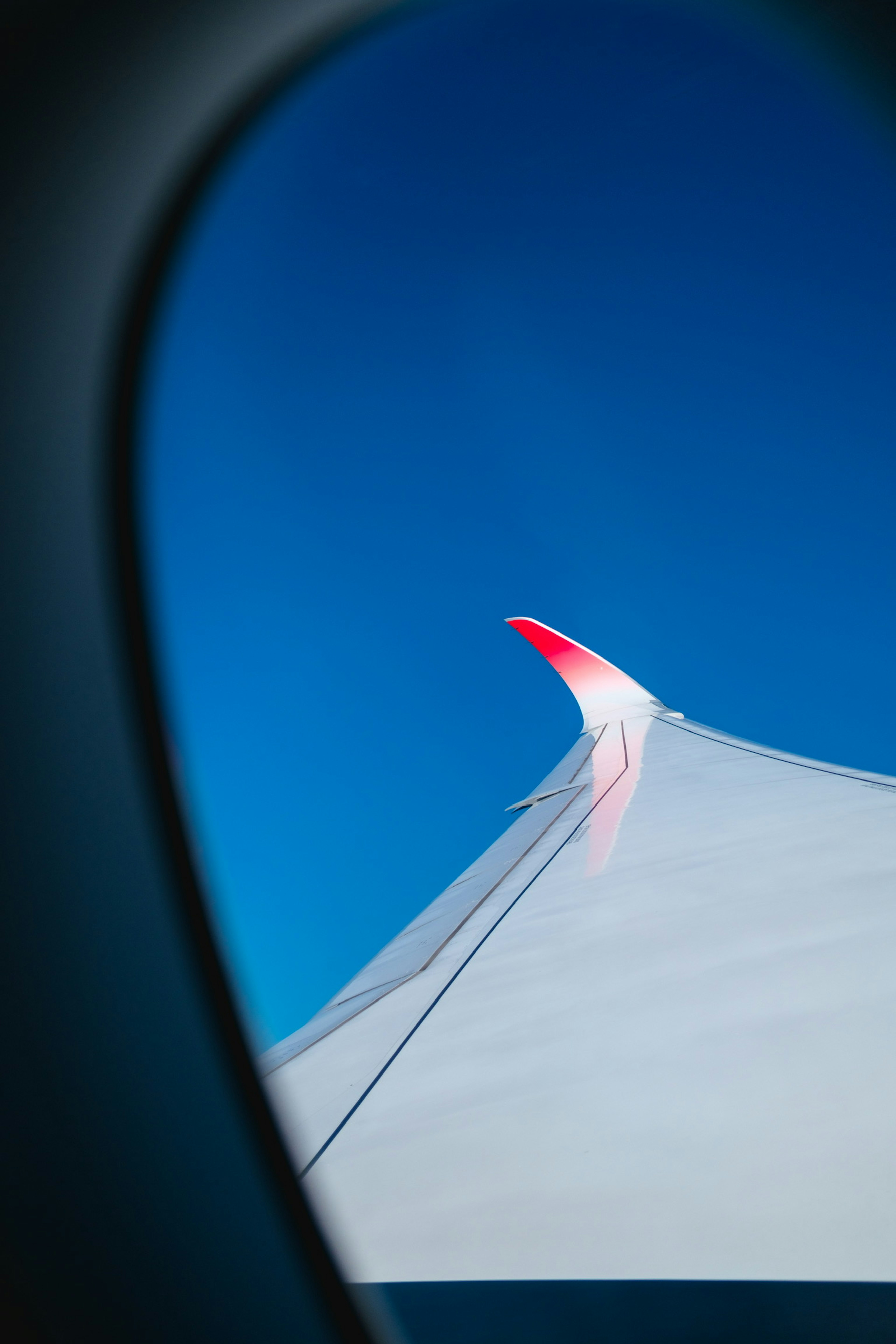 Flugzeugflügelspitze mit rotem Akzent vor blauem Himmel