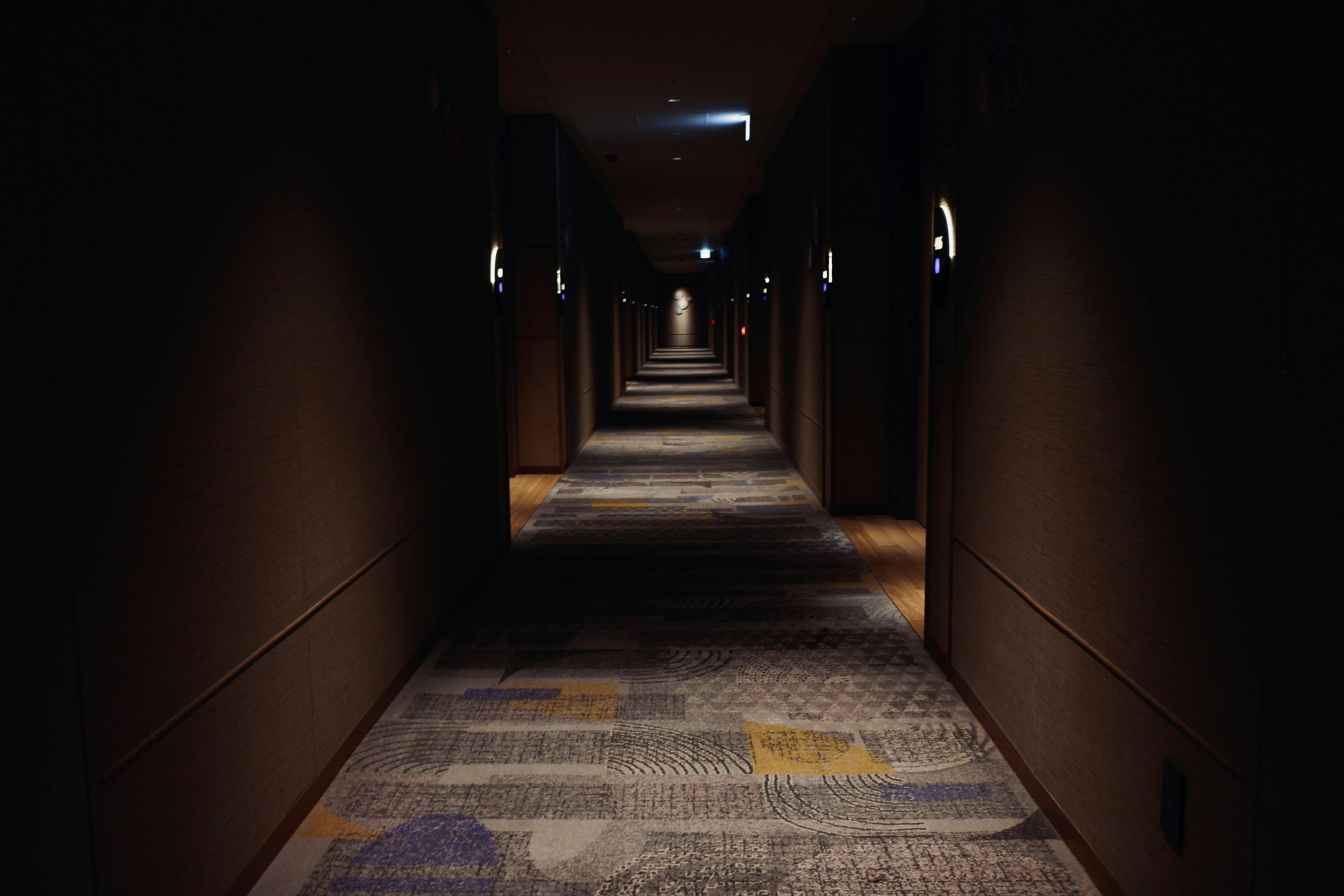 Dimly lit hotel corridor with patterned carpet and wall lights