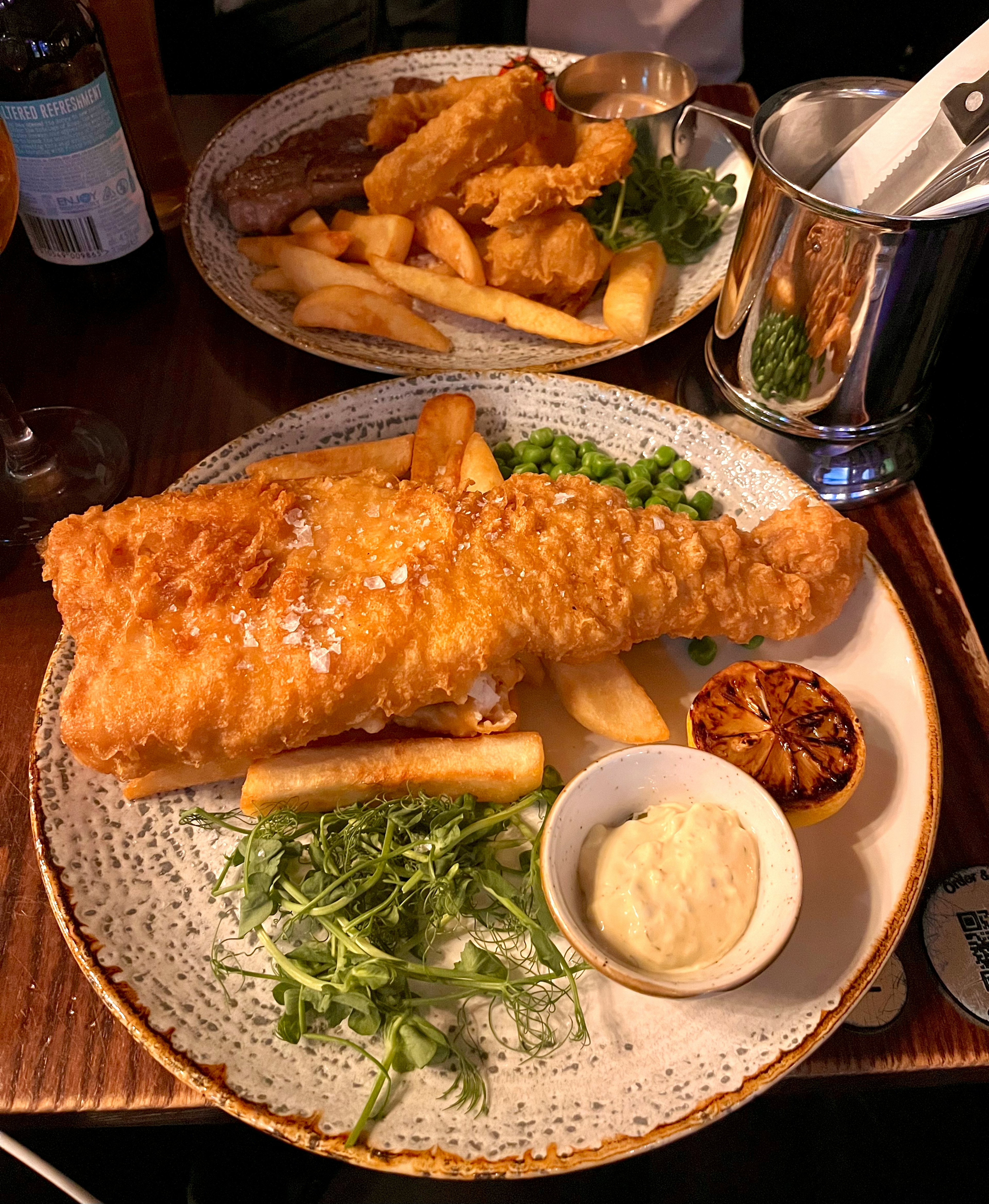 Teller mit knusprigem Fisch und Pommes frites mit grünen Erbsen und Salat daneben