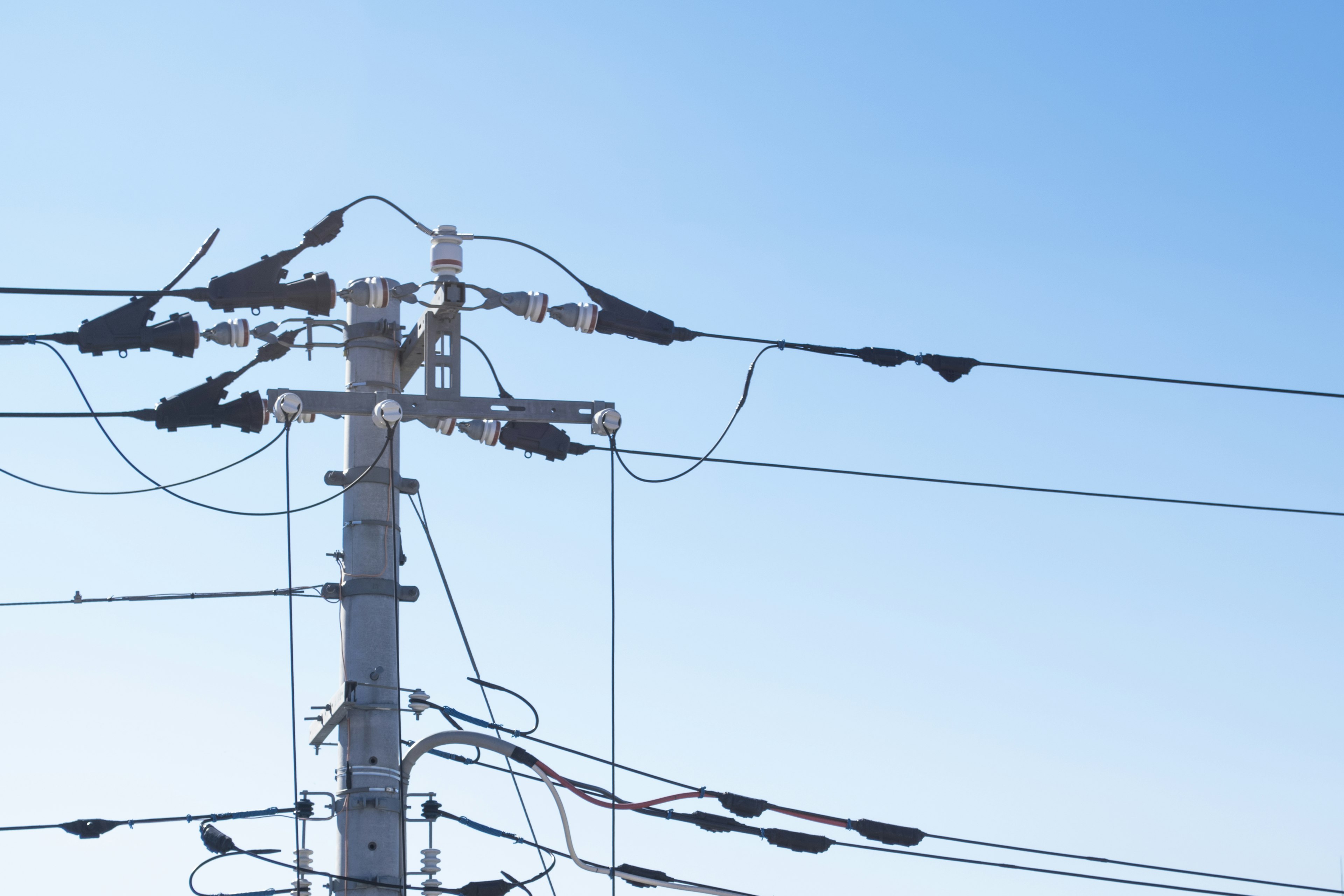 Ein Strommast mit mehreren elektrischen Leitungen vor einem blauen Himmel