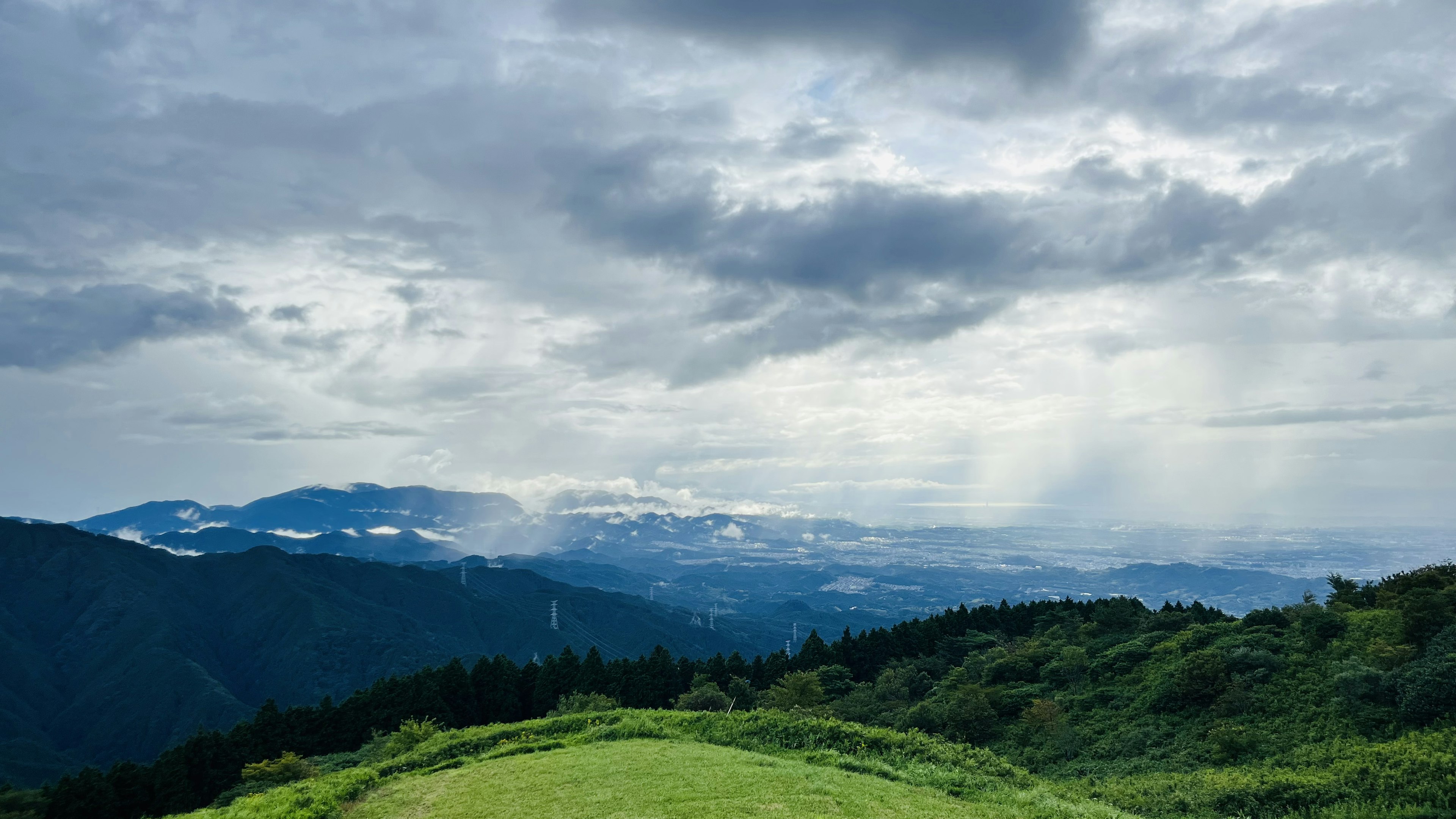 Pemandangan bukit hijau dan gunung di bawah langit mendung