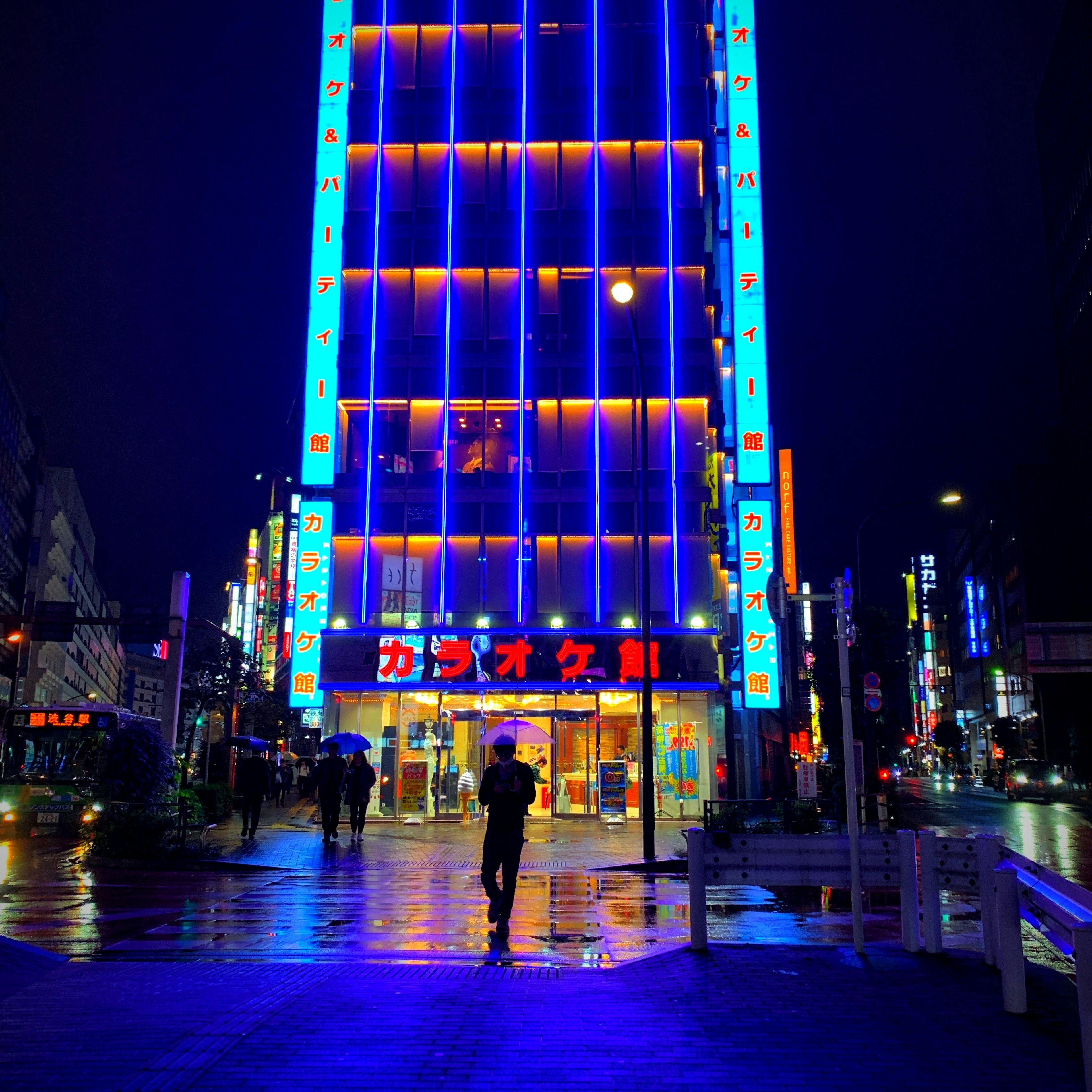 A person standing in front of a brightly lit building with blue and red neon lights at night