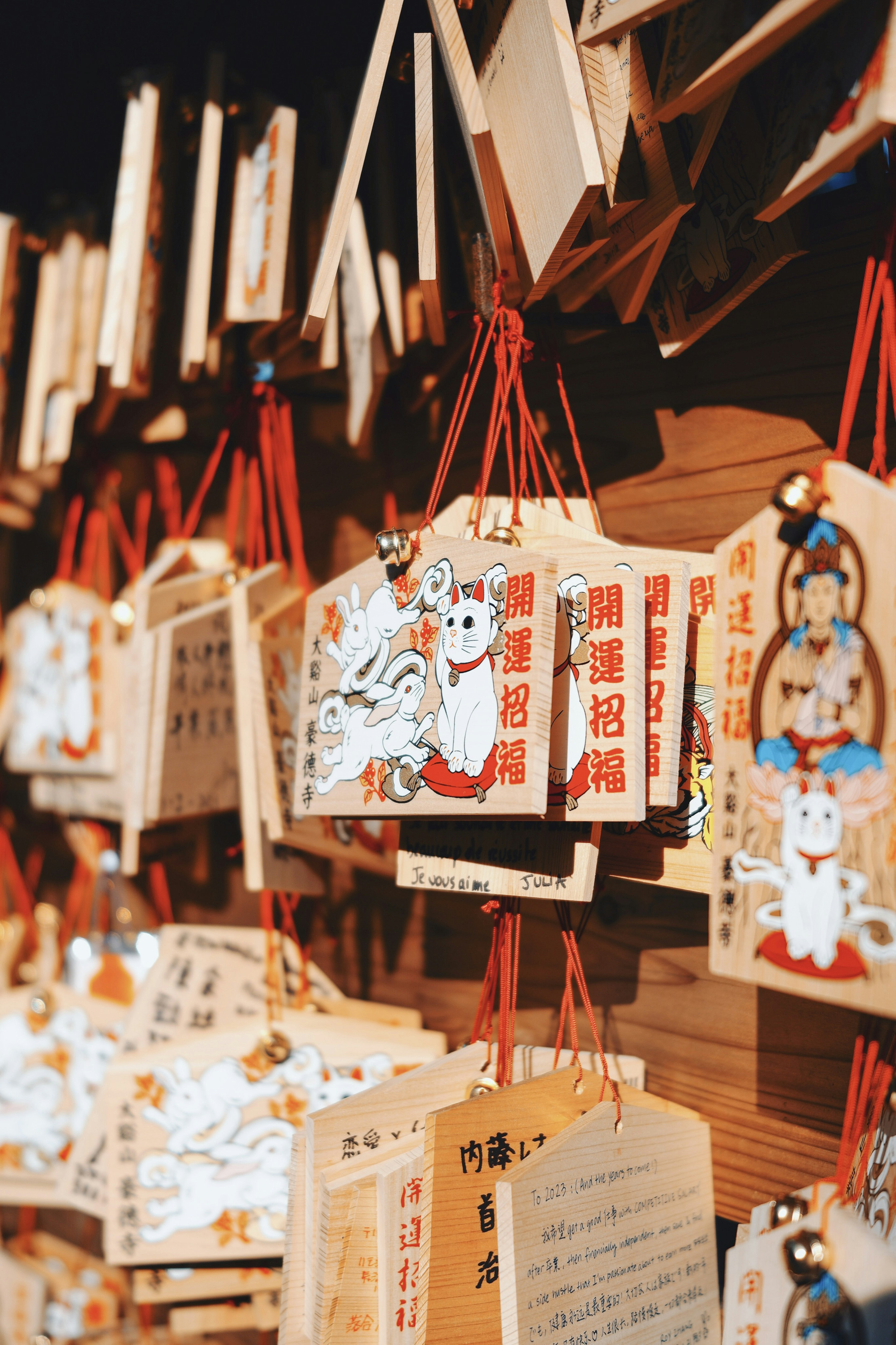 Wooden ema plaques hanging featuring white cats and depictions of deities