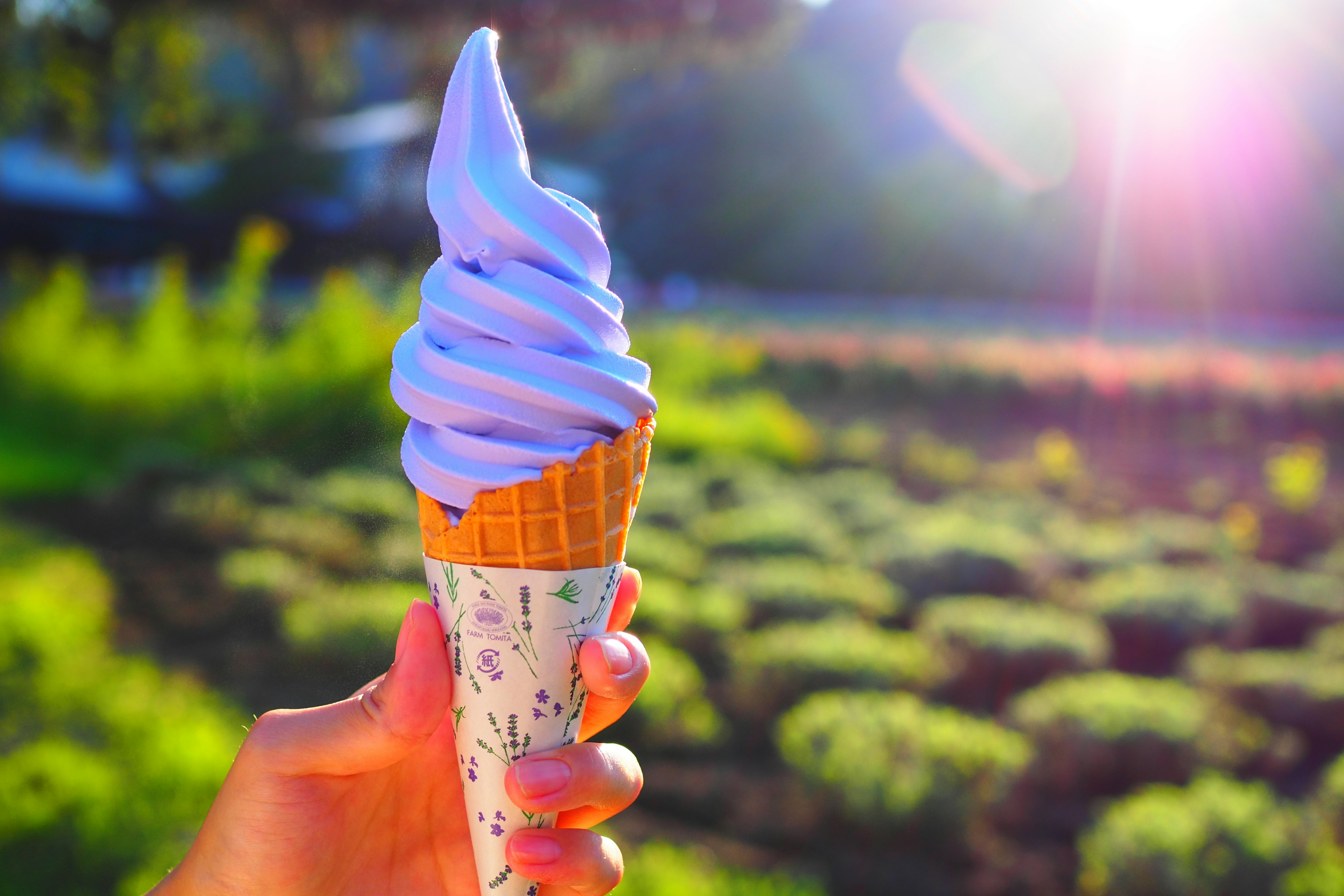 Mano sosteniendo un cono de helado suave morado con un fondo verde