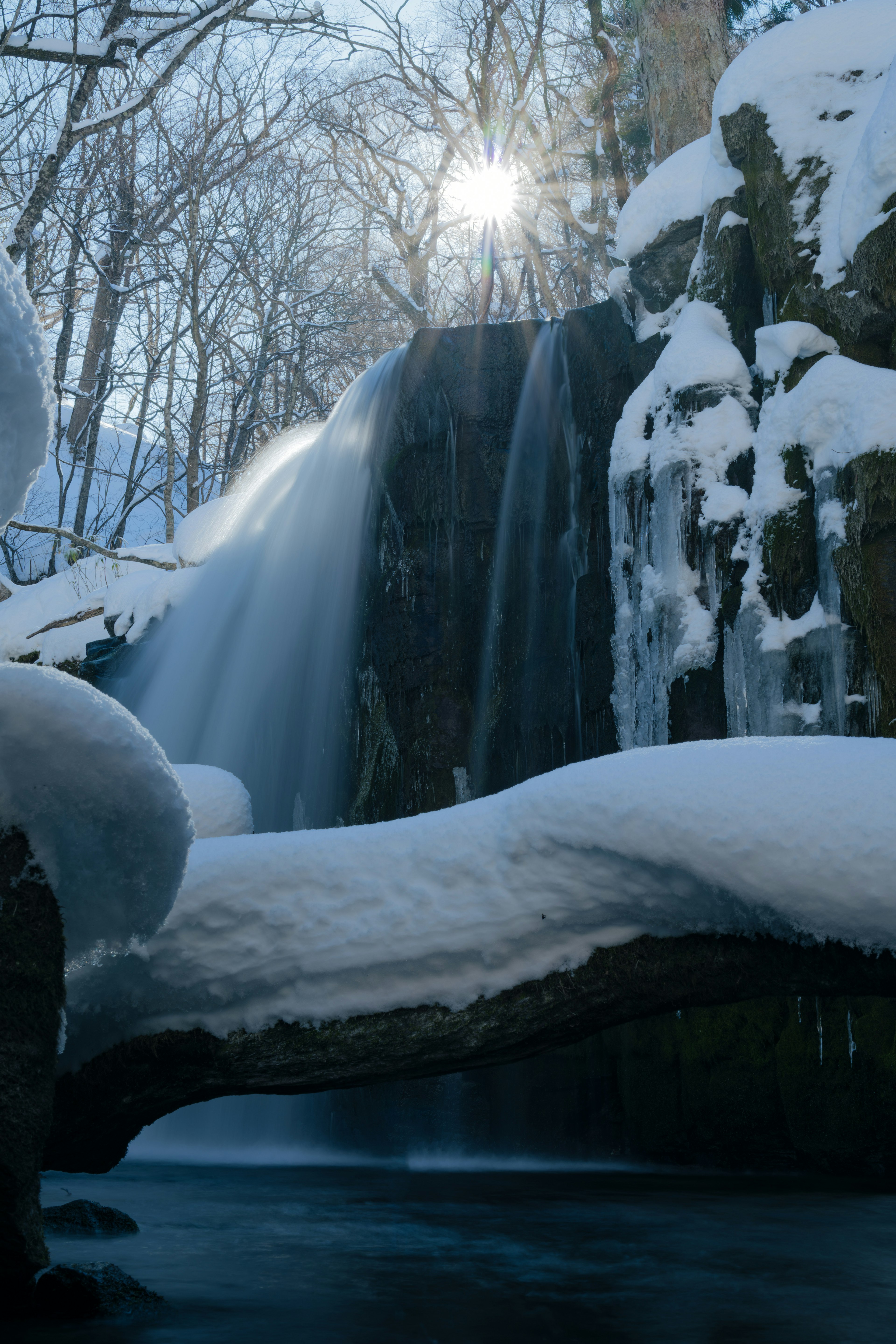 Winterlandschaft mit schneebedecktem Wasserfall und gefrorener Wasseroberfläche bei Sonnenschein