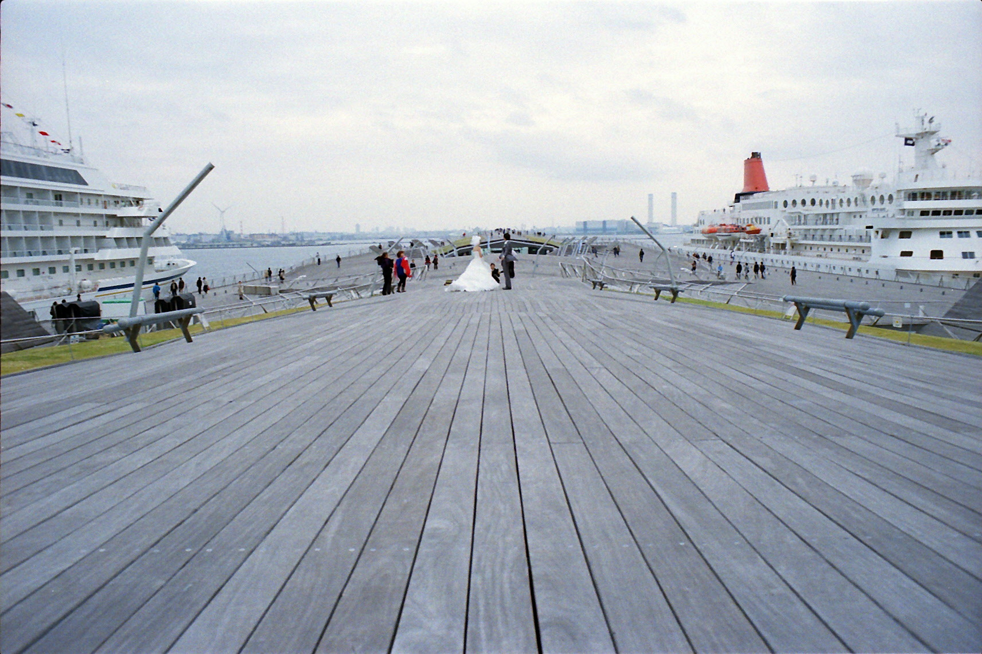 Eine Braut und ihr Partner stehen auf einem Pier in einem Hafen mit Kreuzfahrtschiffen im Hintergrund