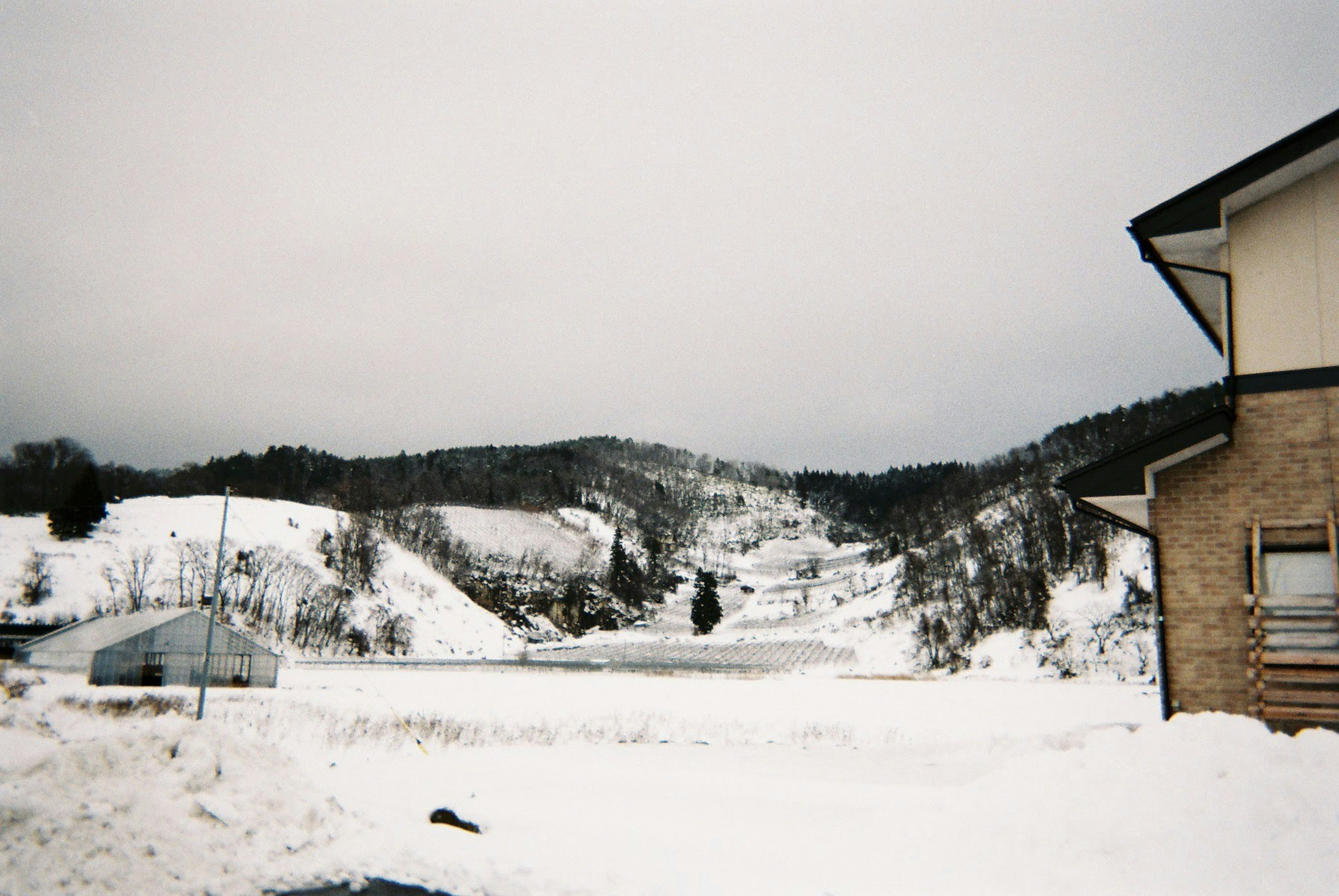 Schneebedeckte Landschaft mit Hügeln und einem Haus