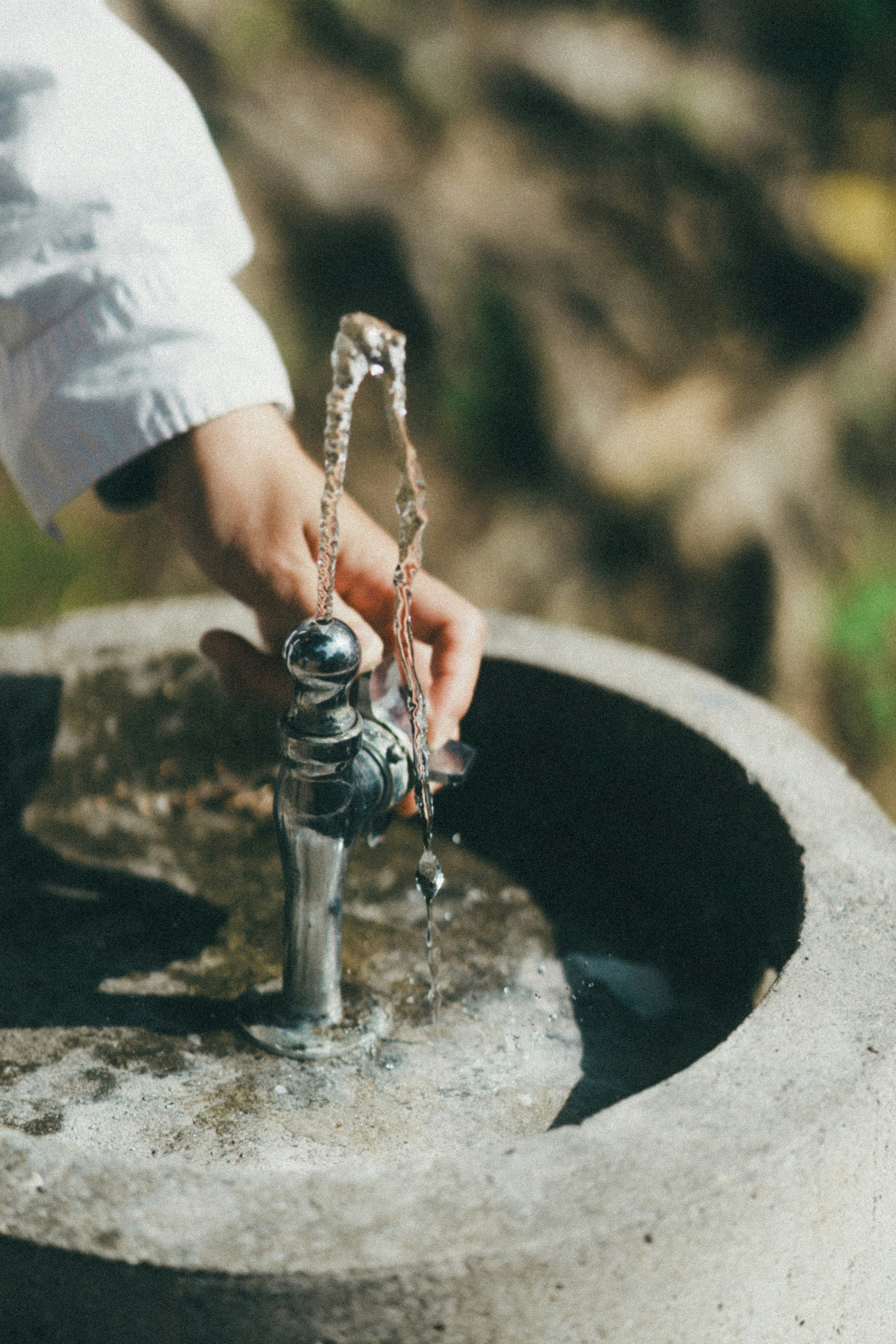 Eine Hand, die einen silbernen Wasserhahn mit fließendem Wasser erreicht