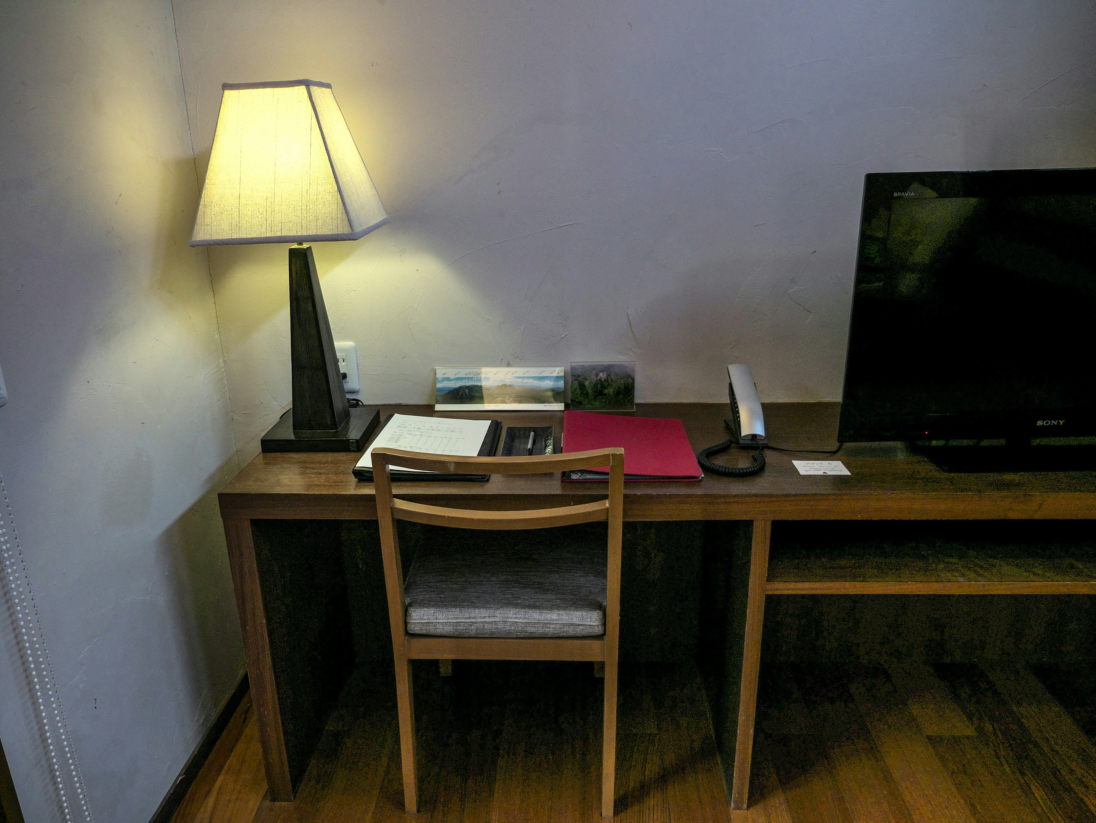 Bureau simple et chaise avec une lampe et une télévision dans un coin de la pièce