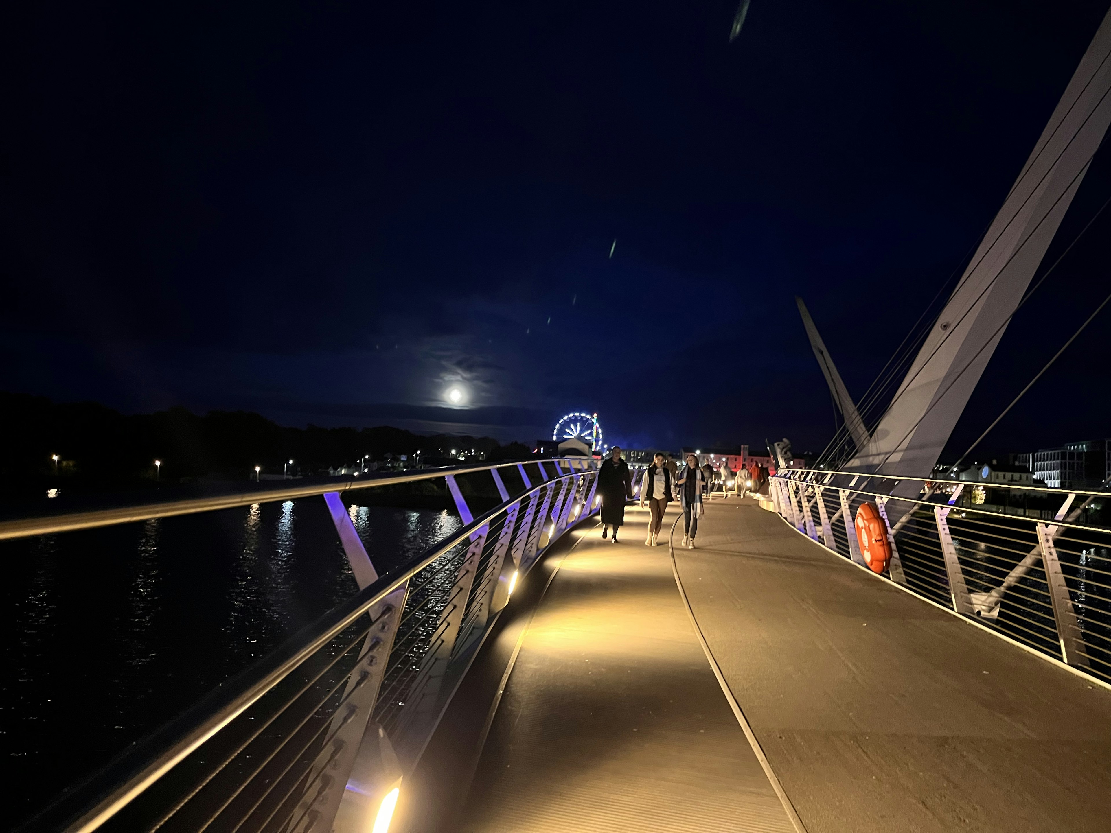 Orang-orang berjalan di jembatan di malam hari dengan cahaya bulan