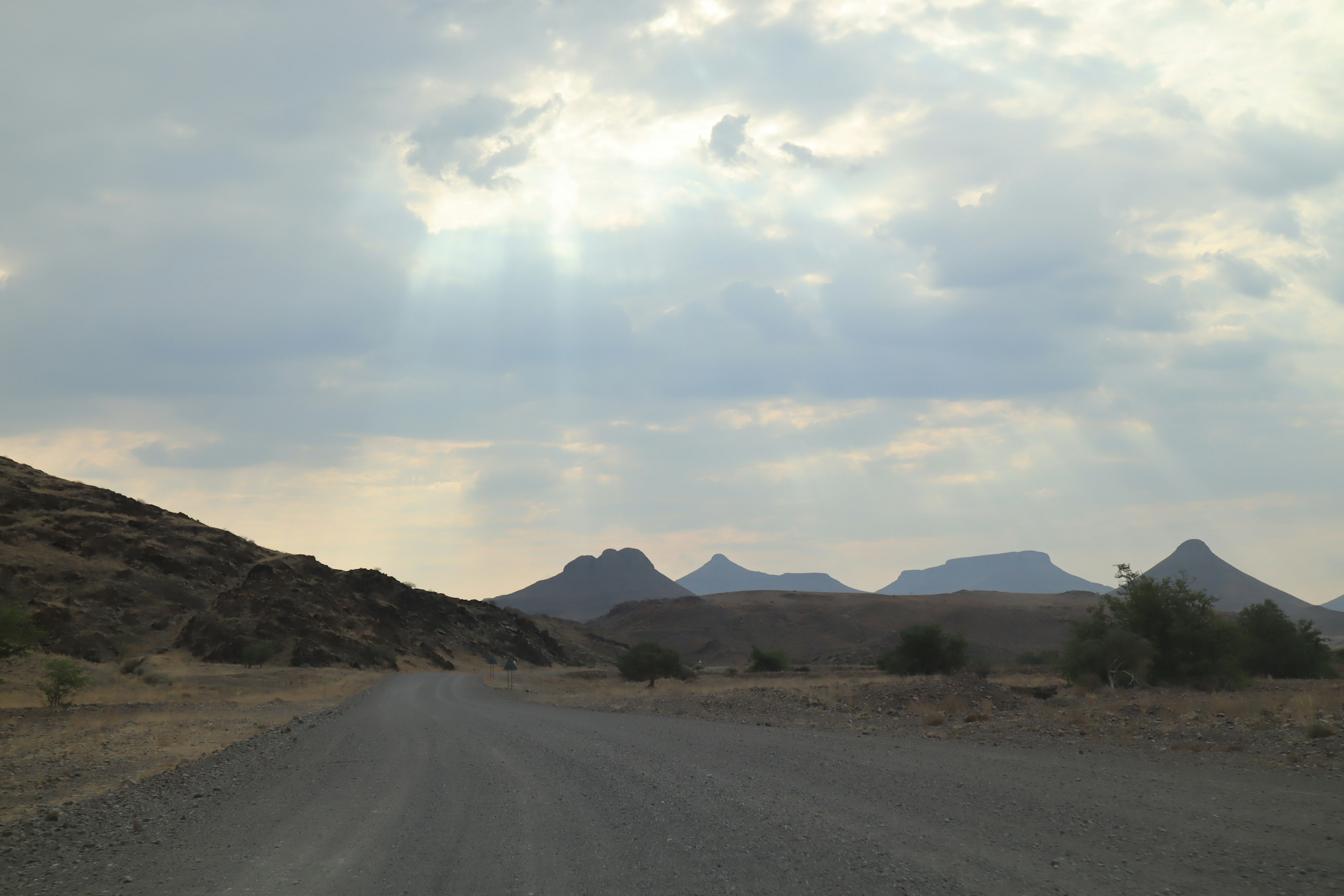 Camino de grava bajo un cielo nublado con montañas distantes