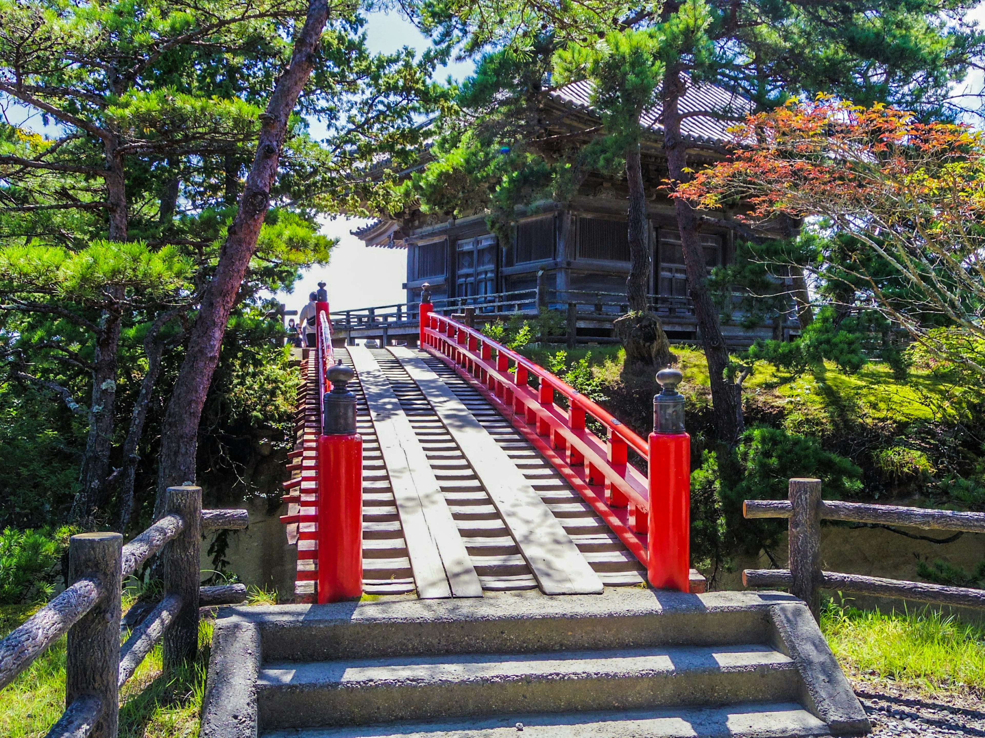 Traditional Japanese building surrounded by trees with a red bridge