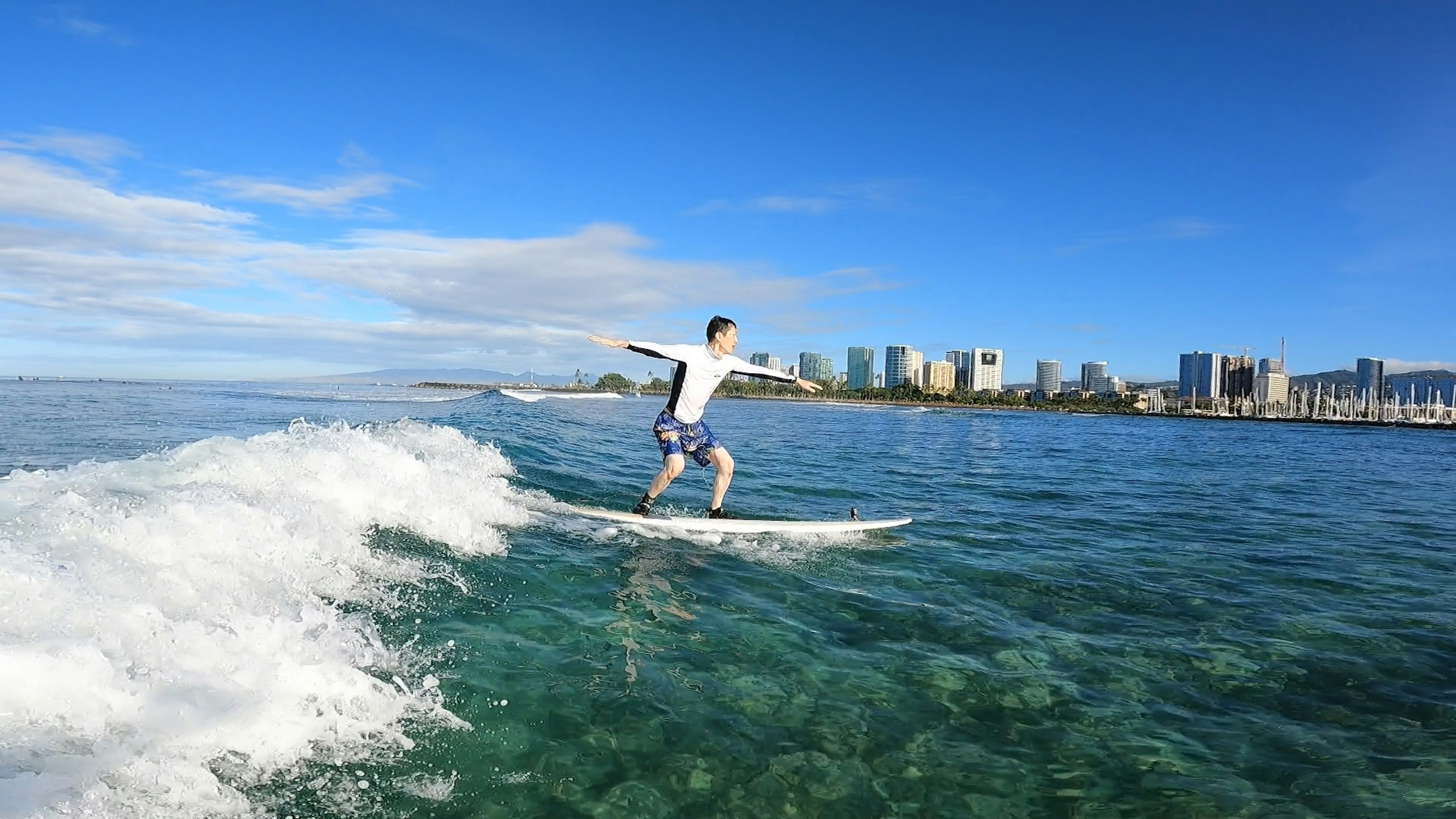 A man surfing on a board riding a wave with a clear blue sky