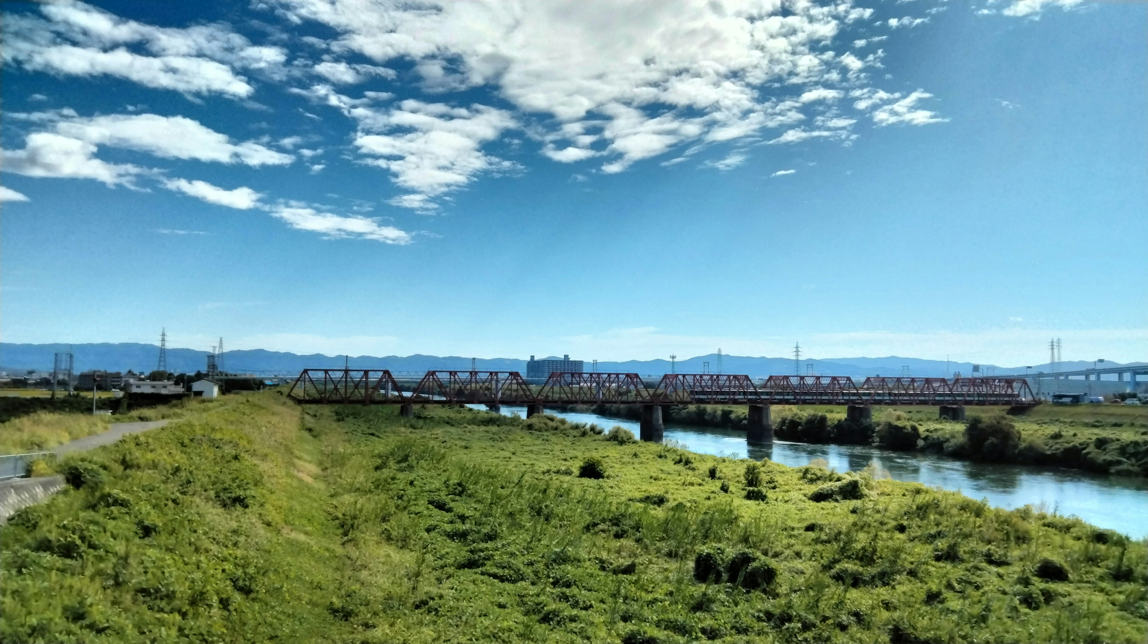 Vista escénica con cielo azul y nubes blancas Pradera verde y río que fluye Puente visible a lo lejos