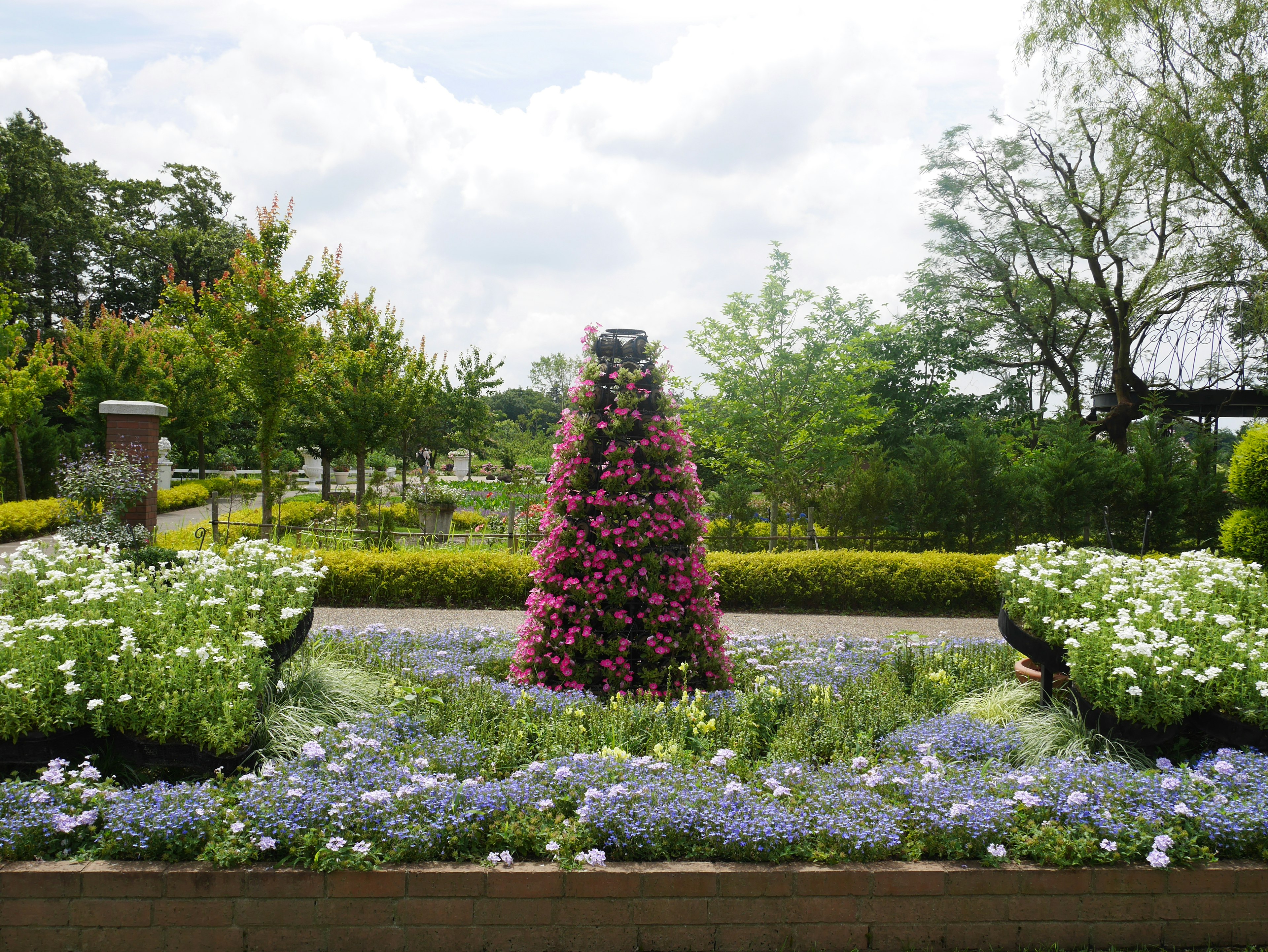 Schöne Gartenansicht mit bunten Blumen ein kegelförmiges Blumenbeet geschmückt mit rosa Blumen umgeben von Grün und blauen Blüten