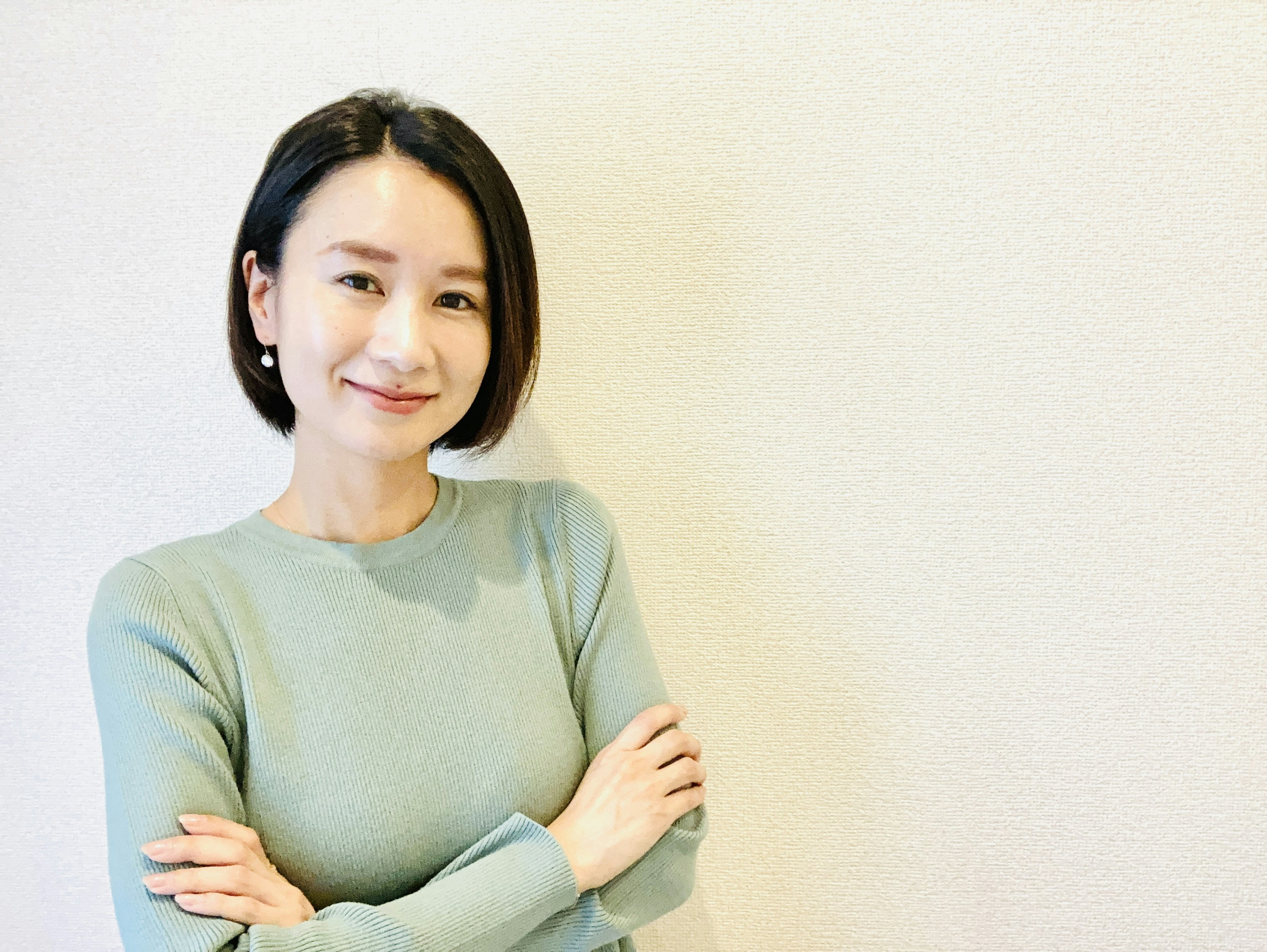 A woman smiling with crossed arms against a light-colored wall