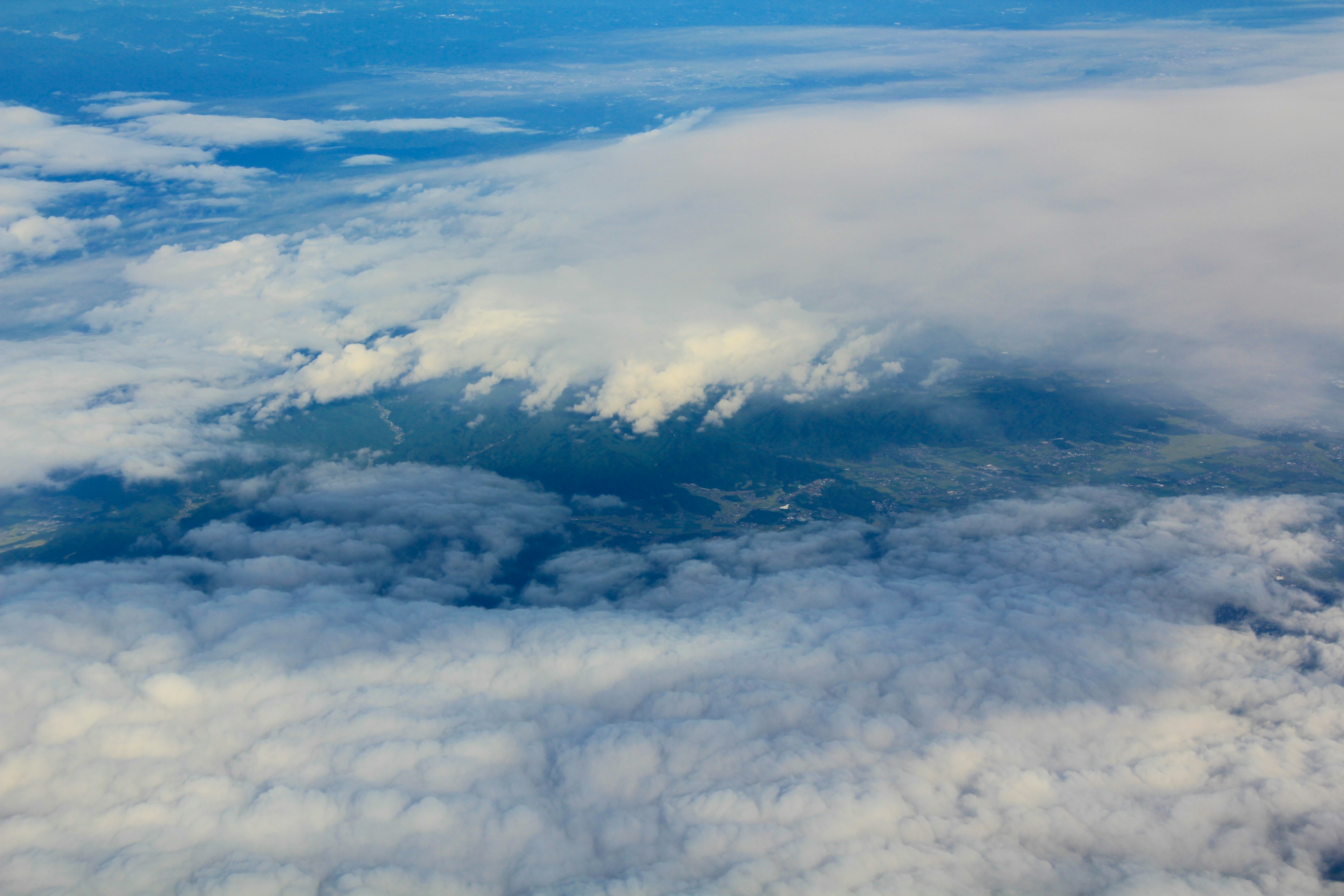 Vista aerea di montagne che emergono dalle nuvole sotto un cielo blu