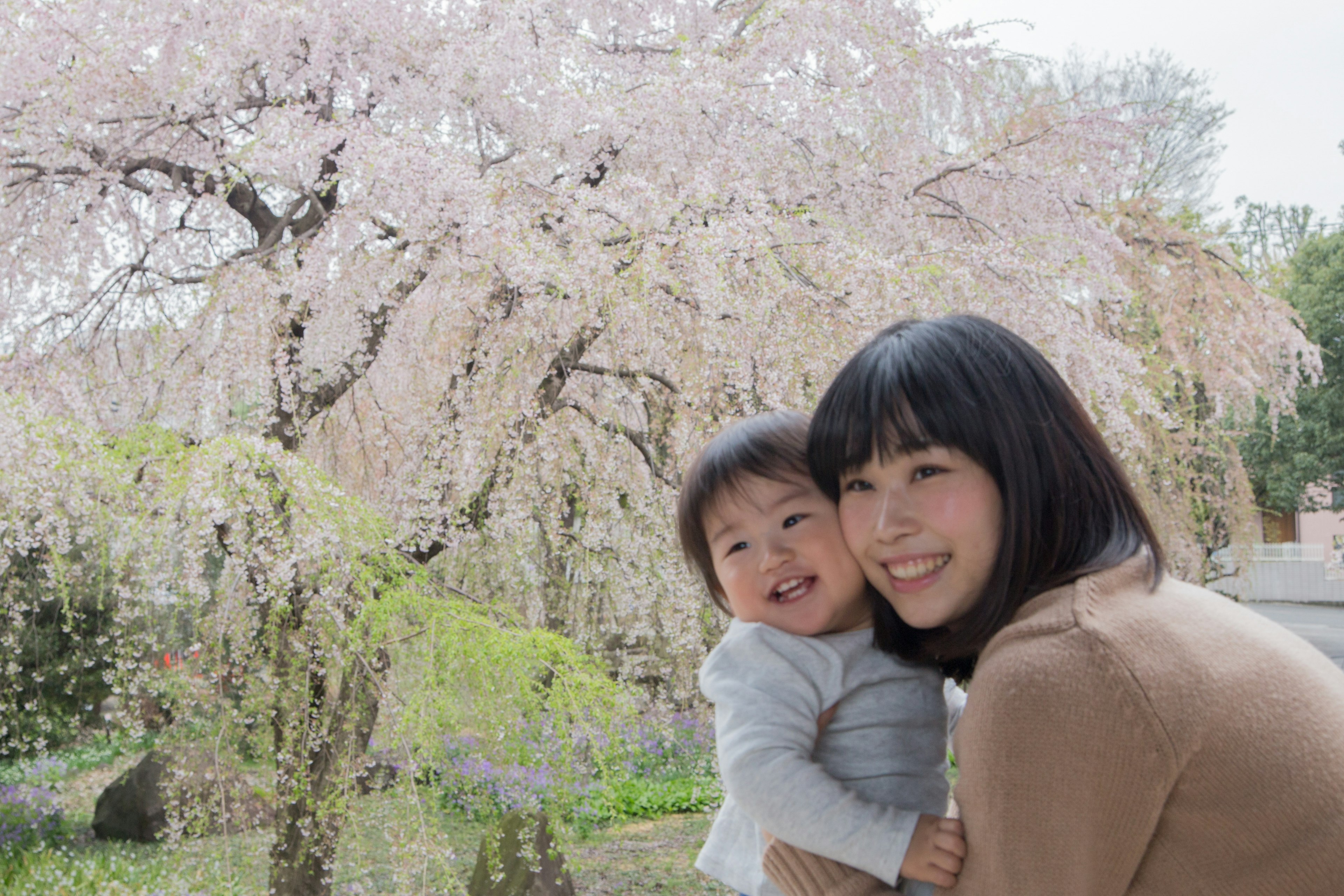 Madre sonriente sosteniendo a un niño frente a un árbol de cerezo en flor