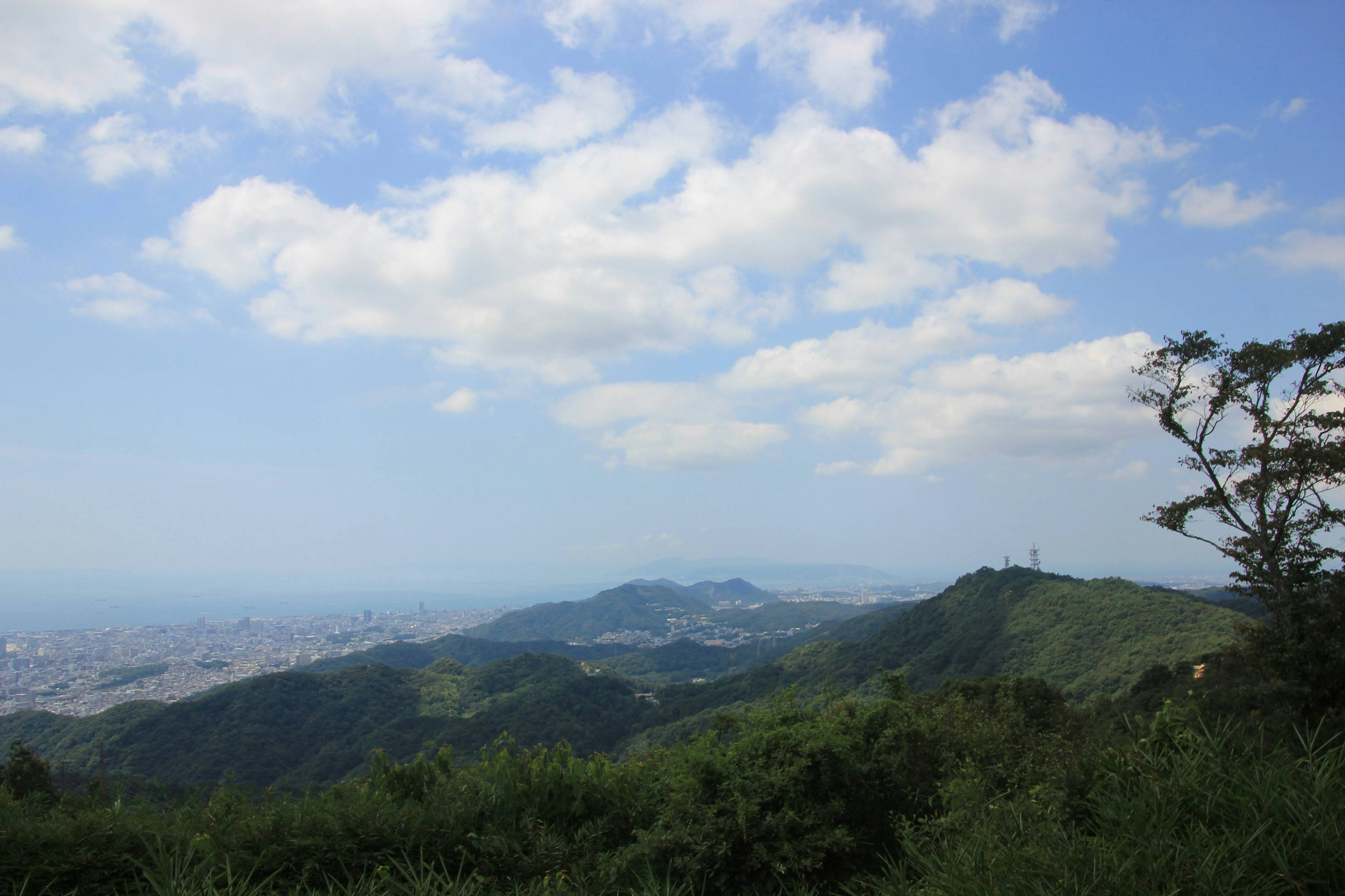 青い空と白い雲が広がる山の風景 緑の丘と遠くの街が見える