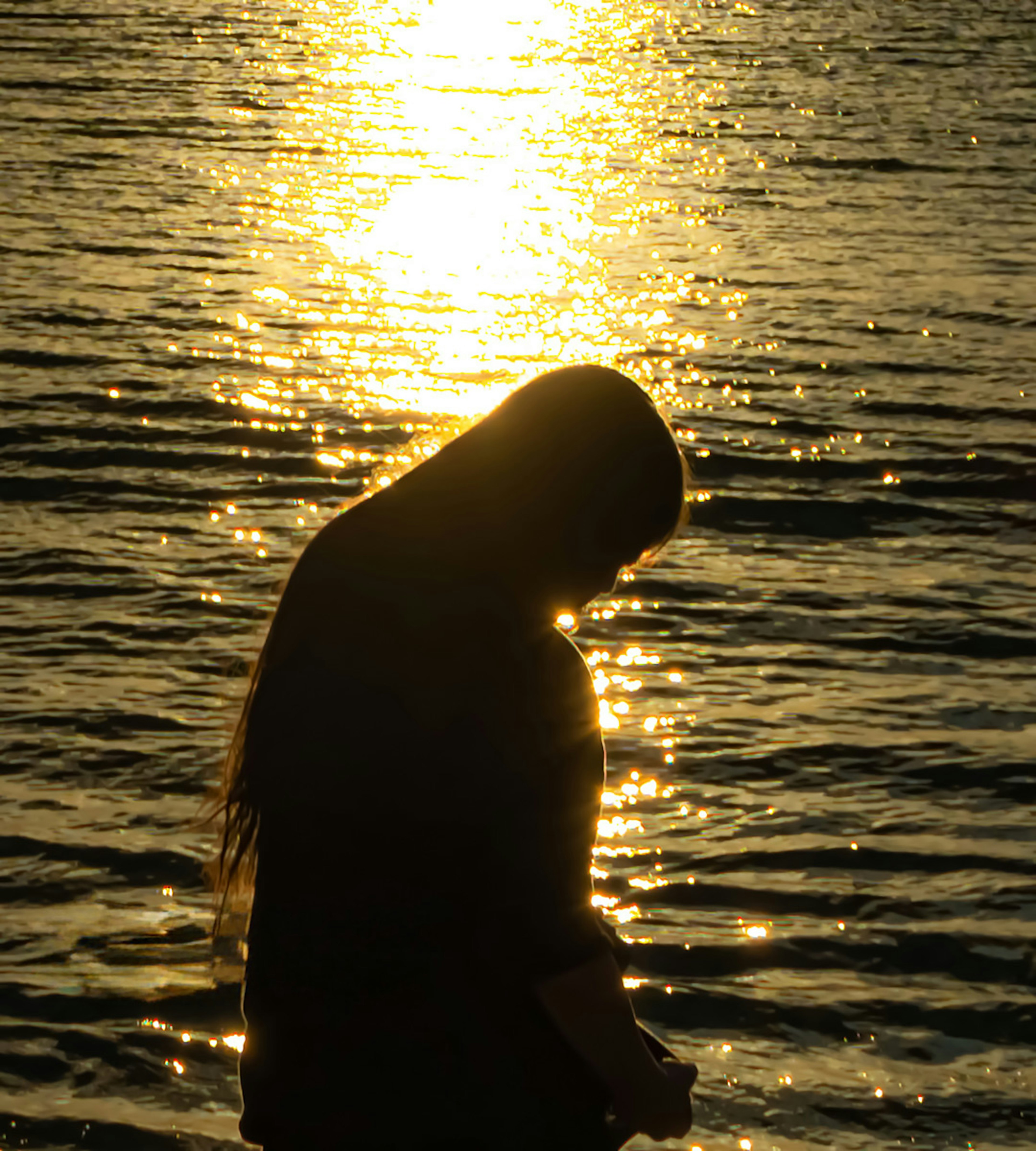 Silueta de una mujer de pie junto al agua que refleja la luz del sol